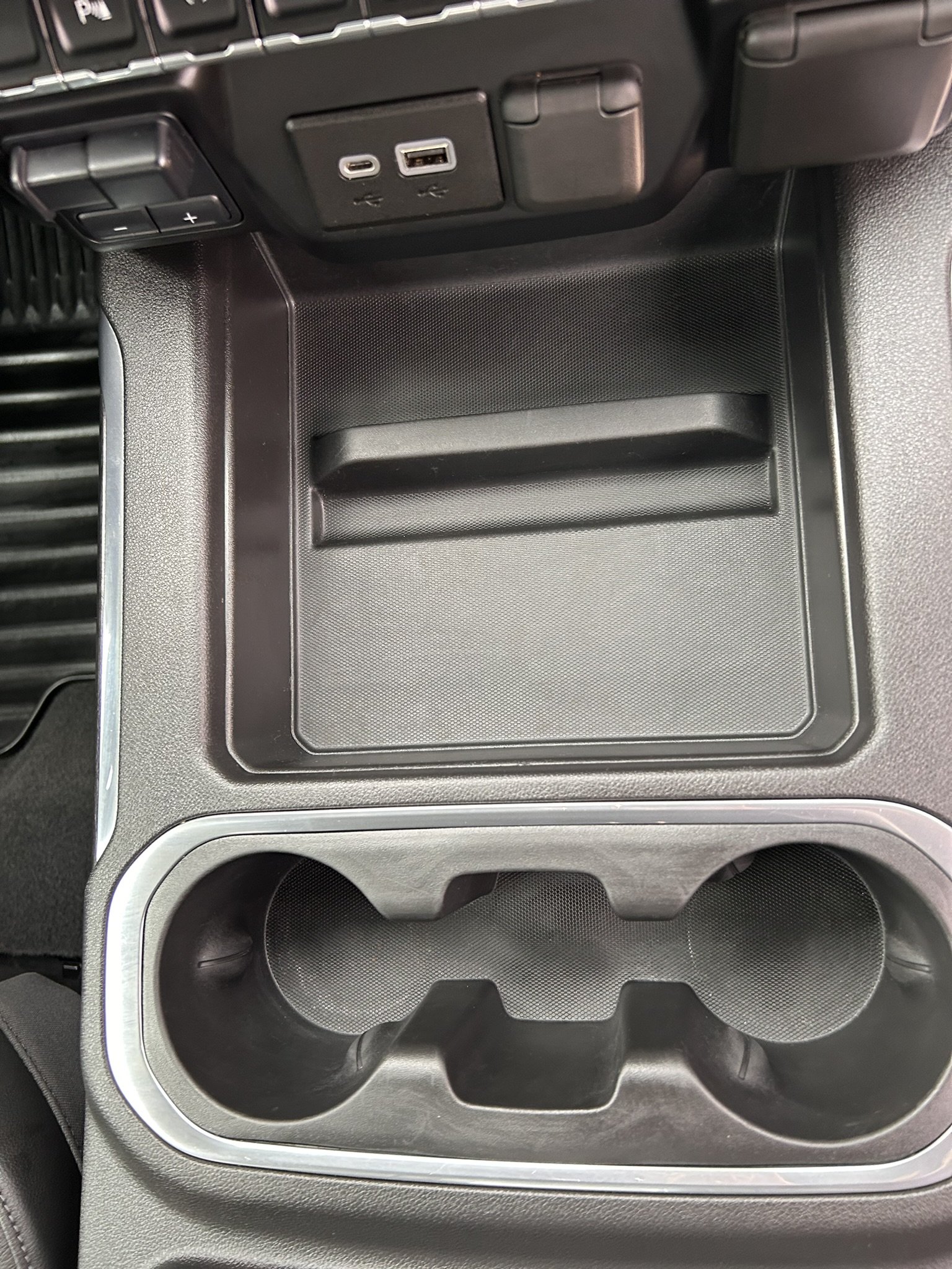 Car's center console with storage compartment, cup holders, and USB ports.