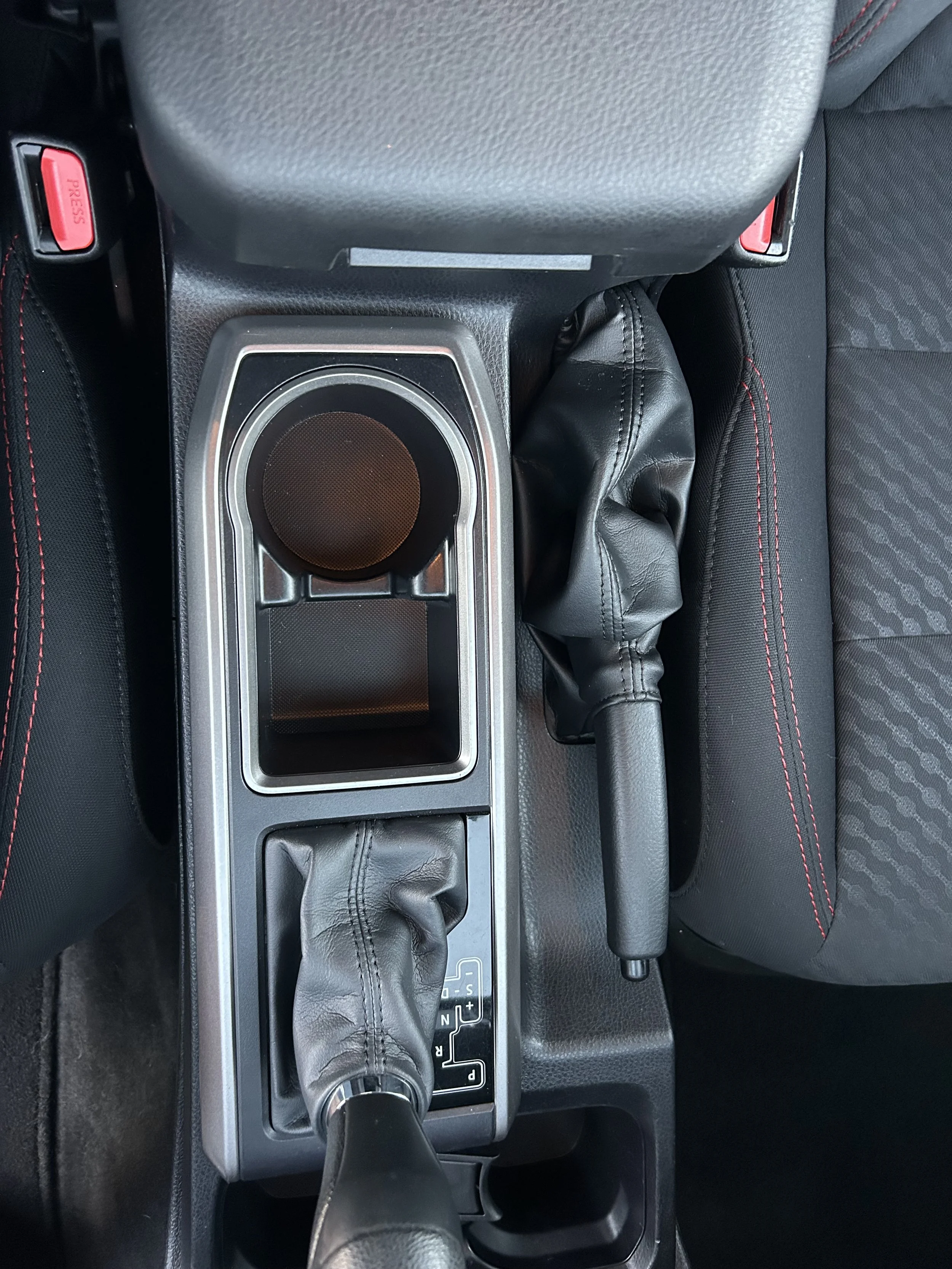 Center console of a car showing a gear shifter with a leather boot, an empty cup holder, and a parking brake.