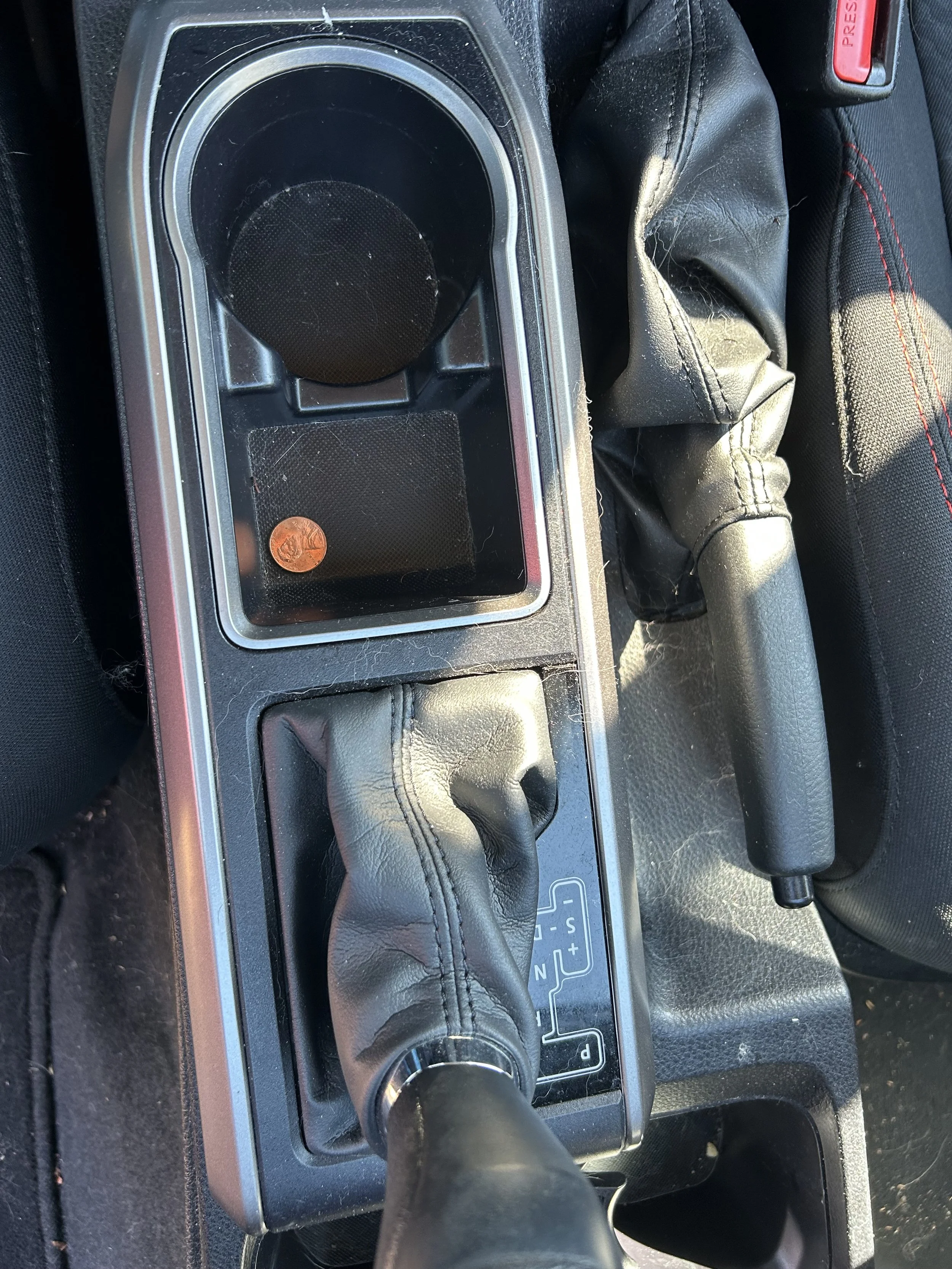 Center console of a car showing a cup holder with a penny, gear shift, and handbrake.