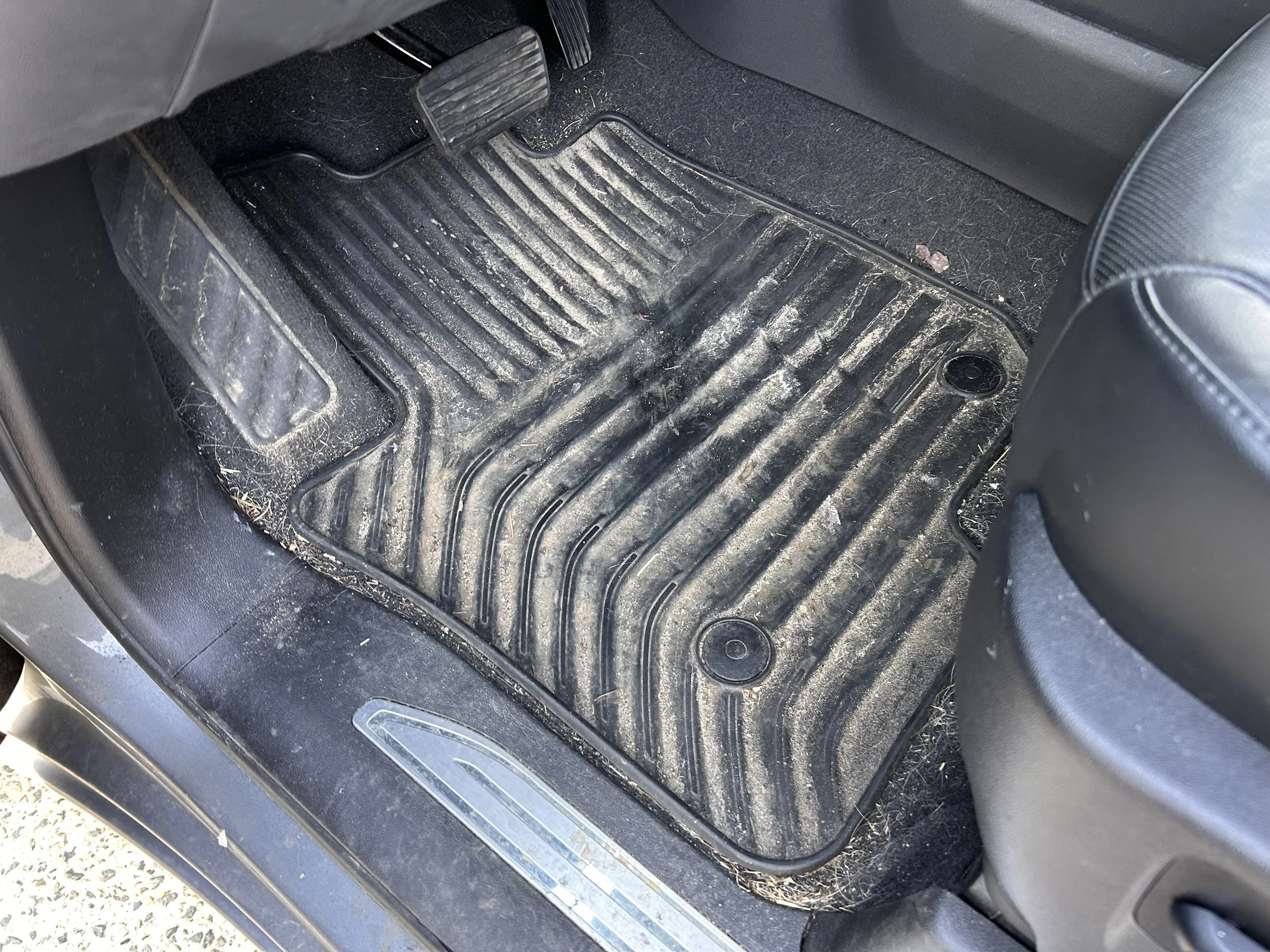 Dirty car floor mat with dust, dirt, and debris inside a vehicle.