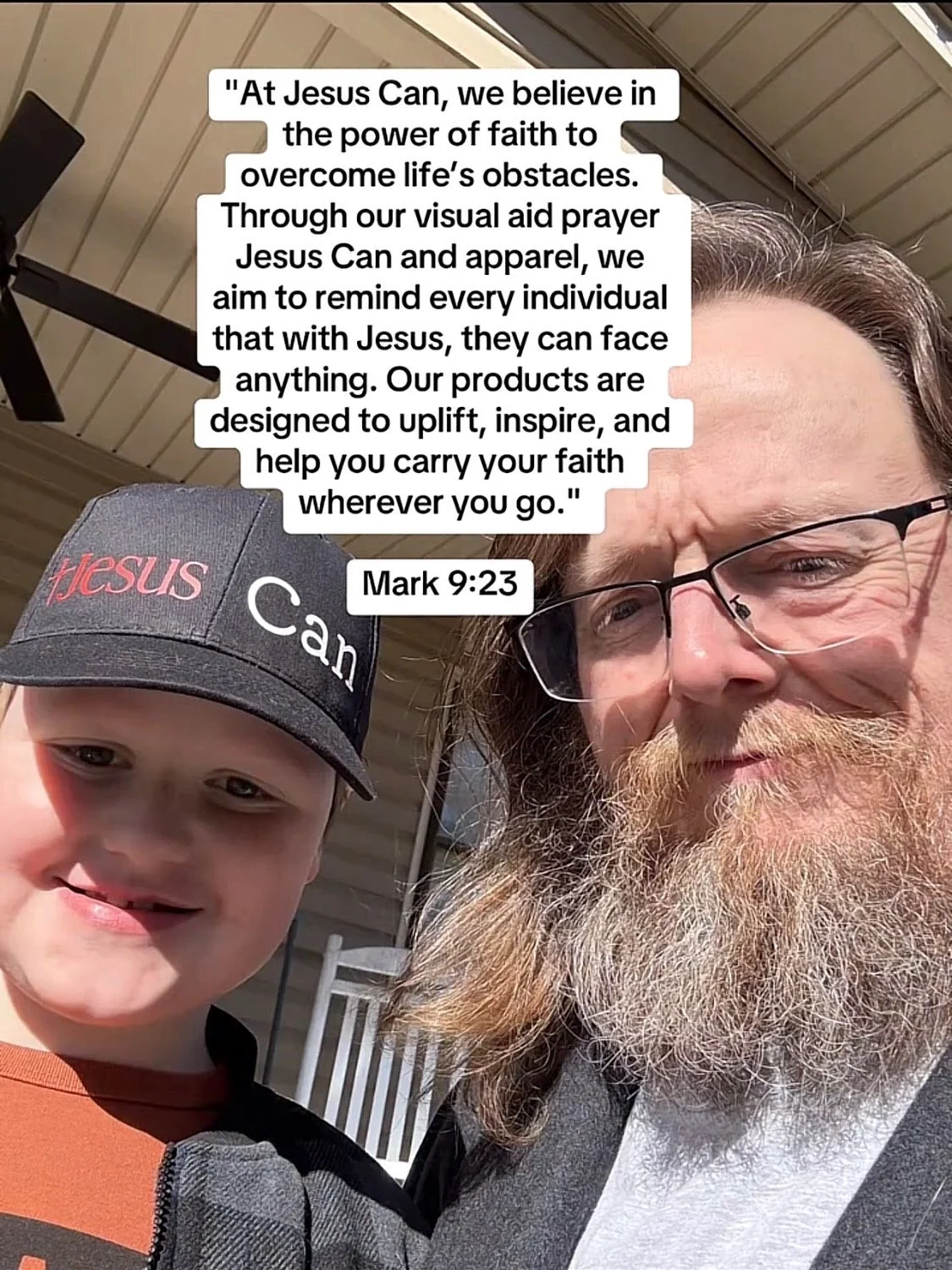 A man with long hair and a beard wearing glasses, and a young boy wearing a baseball cap with the words 'Jesus Can' on it, taking a selfie outdoors on a porch.