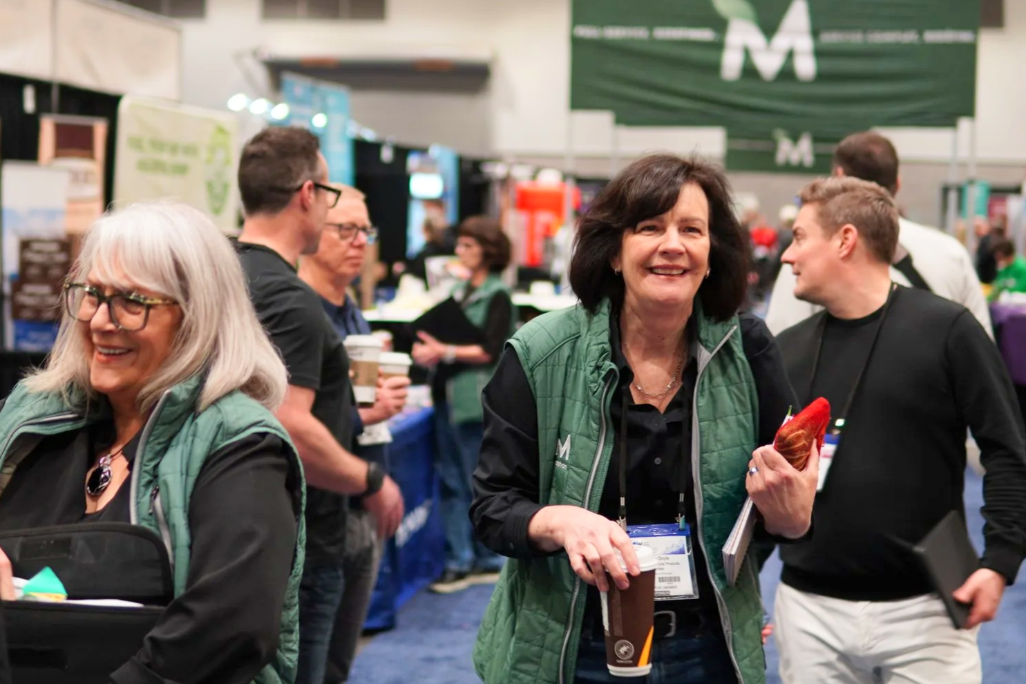 a woman smiling and walking towards the camera while holding a coffee and papers