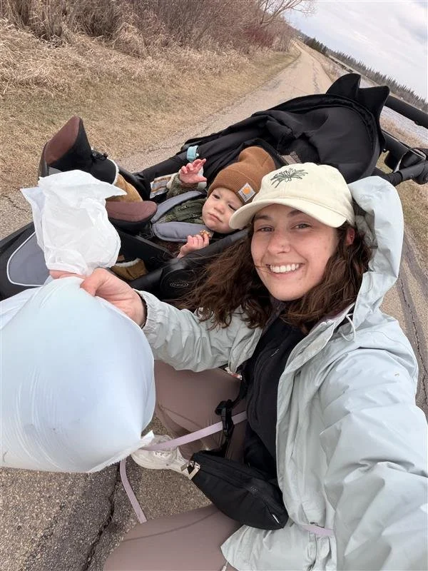 a woman and a baby on a sidewalk smiling and holding up a plastic bag