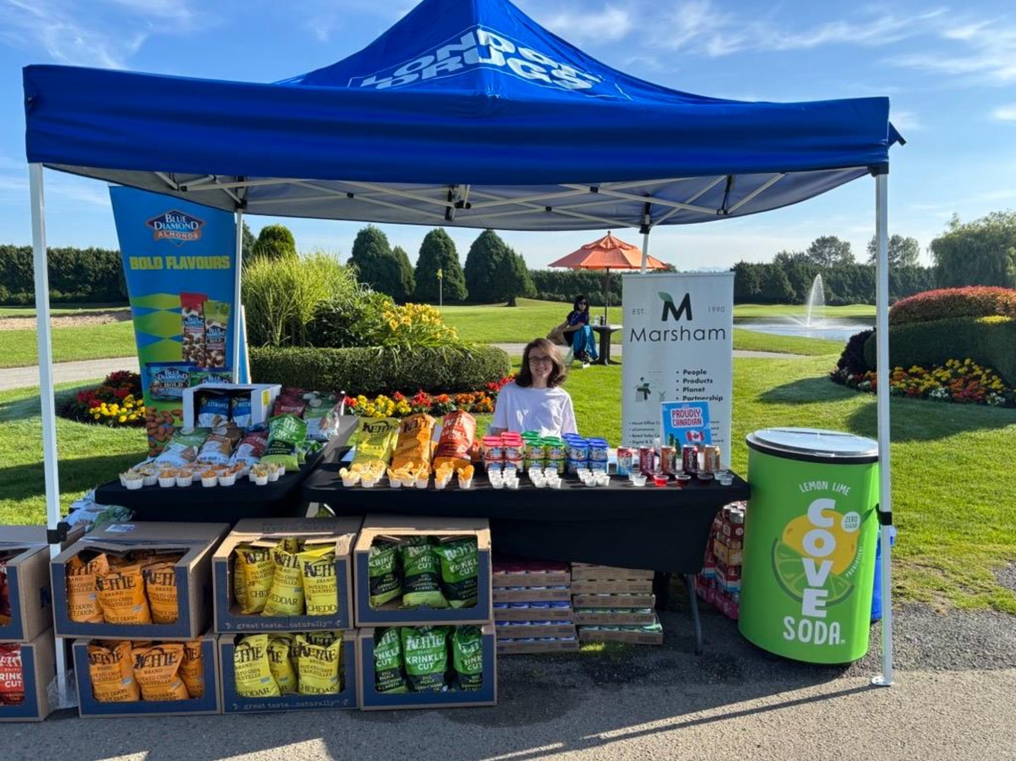a woman sitting under a tent and surrounded by samples of Kettle chips