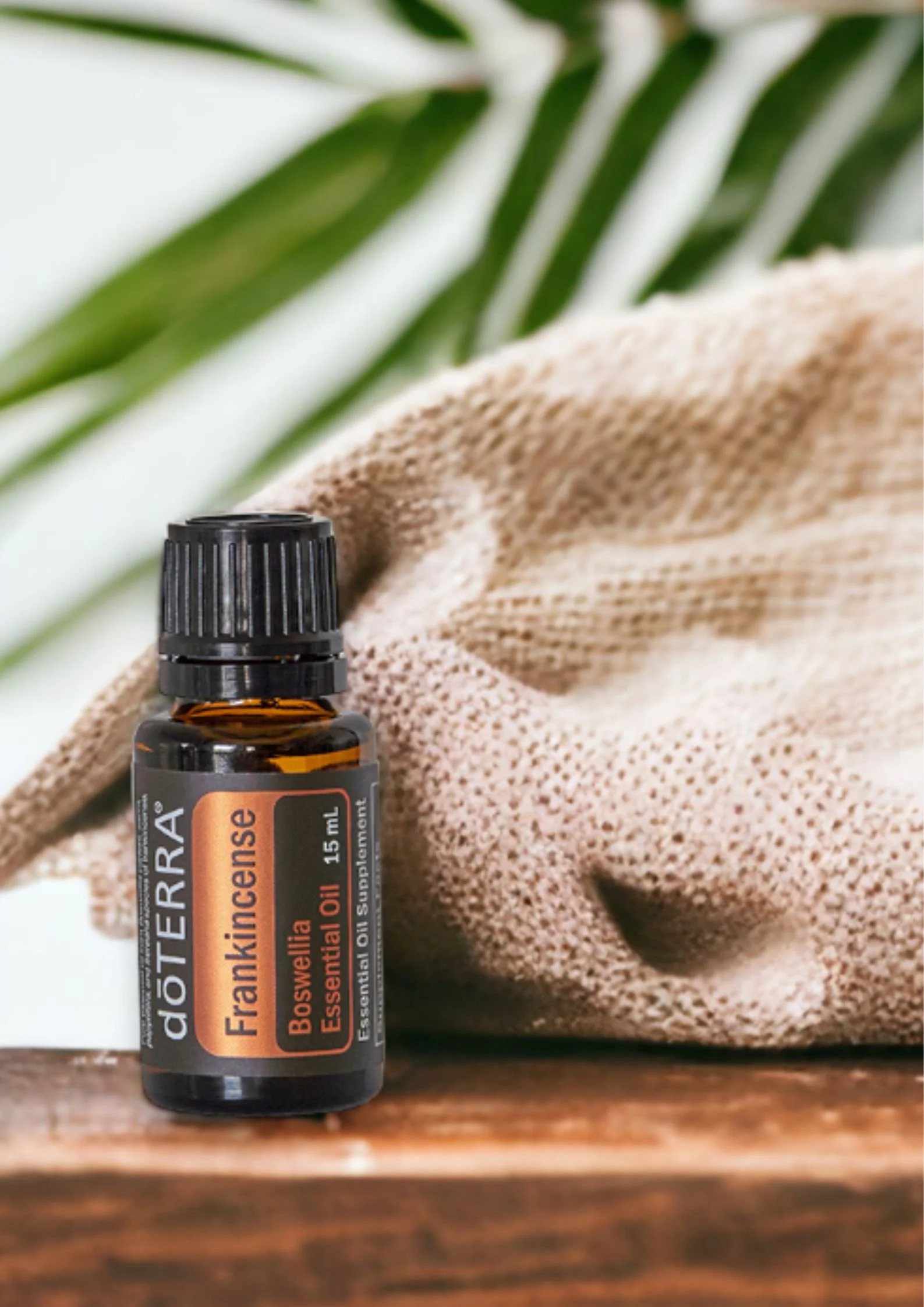 Boccetta di olio essenziale di incenso Frankincense doTERRA su base di legno con sacchetto di juta dietro e foglie sullo sfondo - Silvia Pagliarini