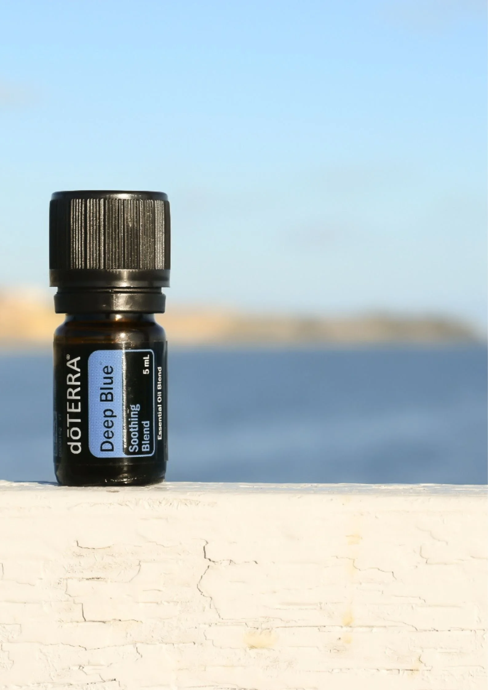 Boccetta di miscela lenitiva Deep Blue  doTERRA su un muretto con il mare sullo sfondo - Silvia Pagliarini
