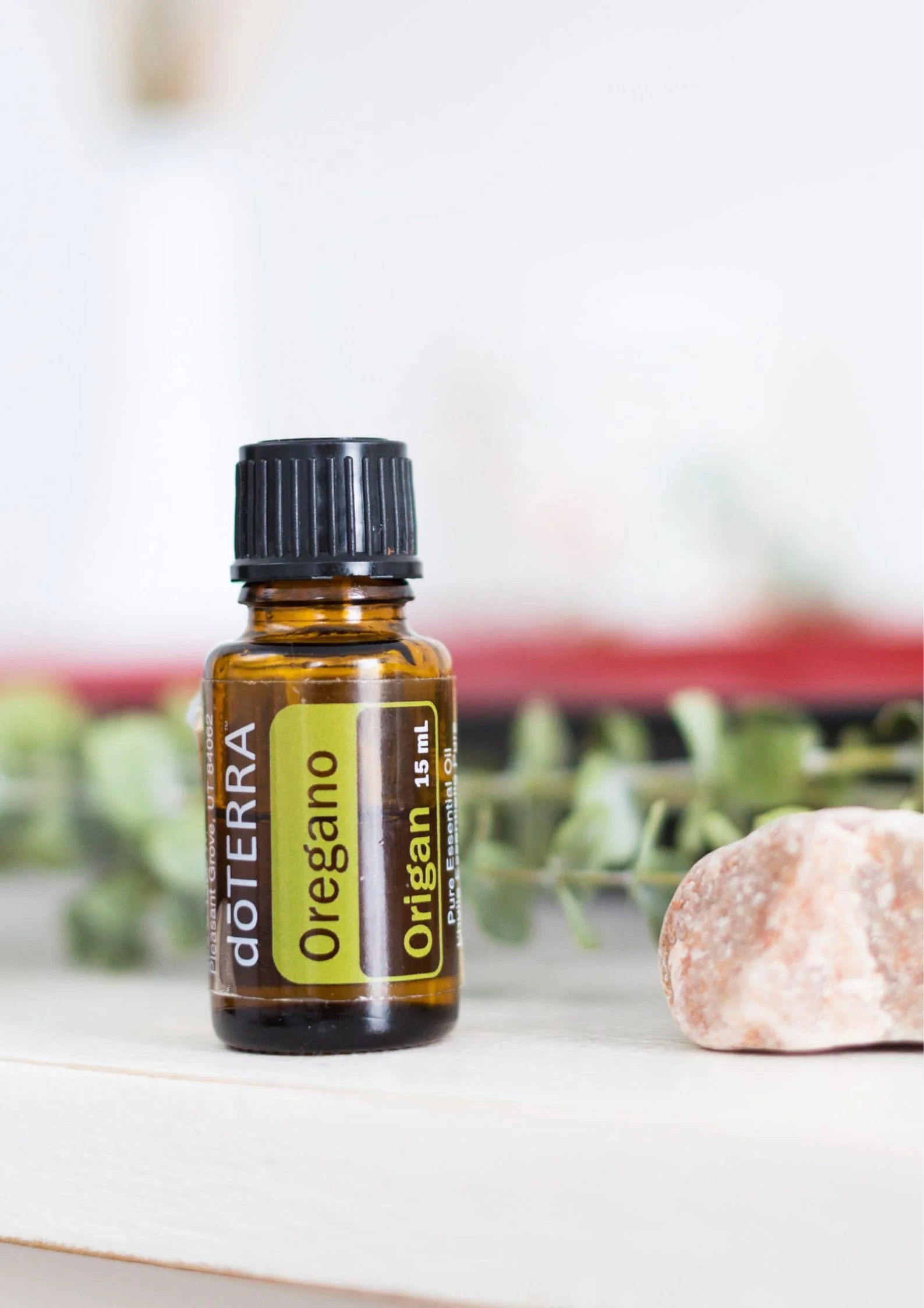 Boccetta di olio essenziale di Origano doTERRA su base chiara con una pietra di fianco e foglie di origano sullo sfondo - Silvia Pagliarini