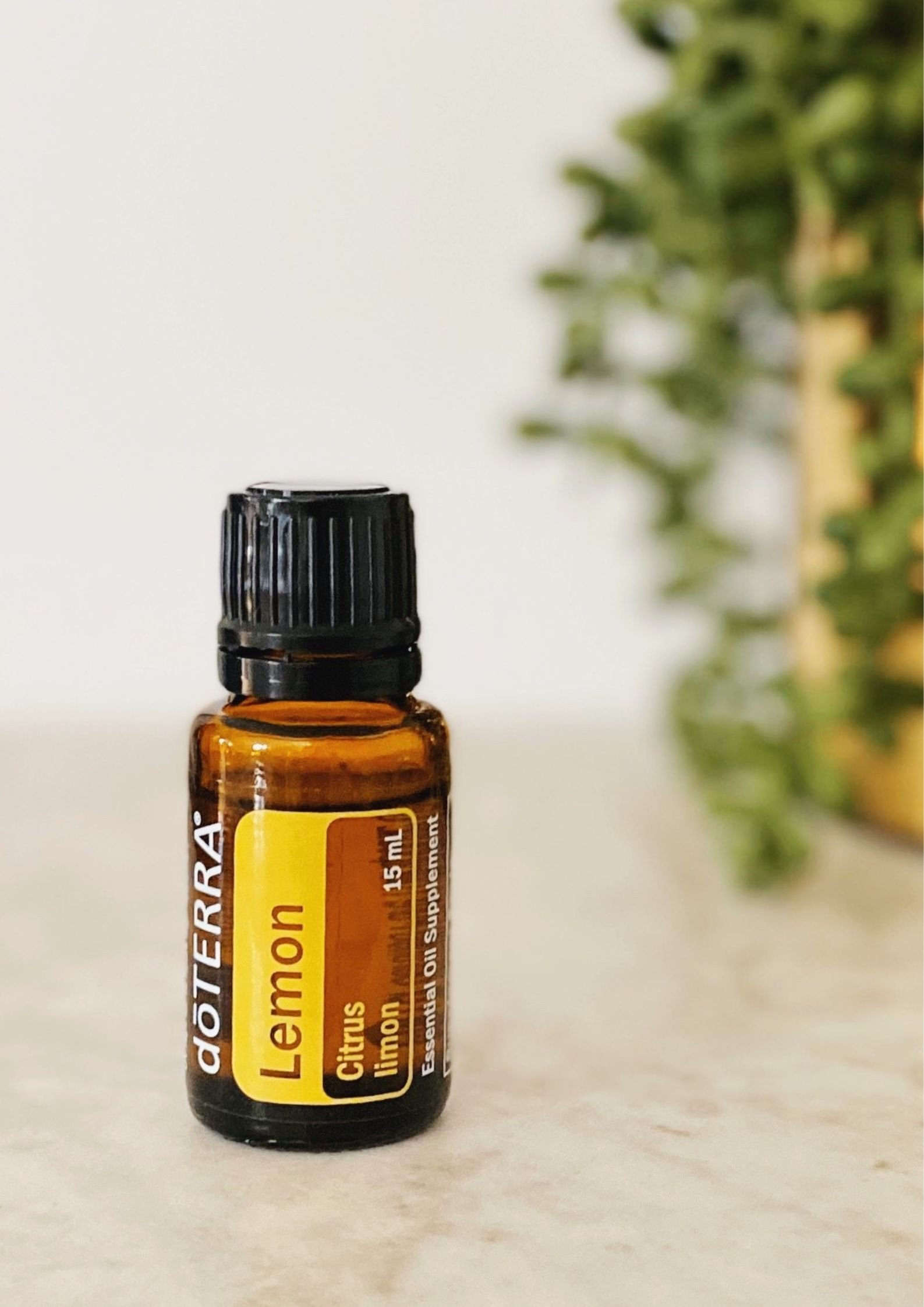 Boccetta di olio essenziale di Limone doTERRA su base di marmo e una pianta in un vaso dorato sfuocata sullo sfondo - Silvia Pagliarini