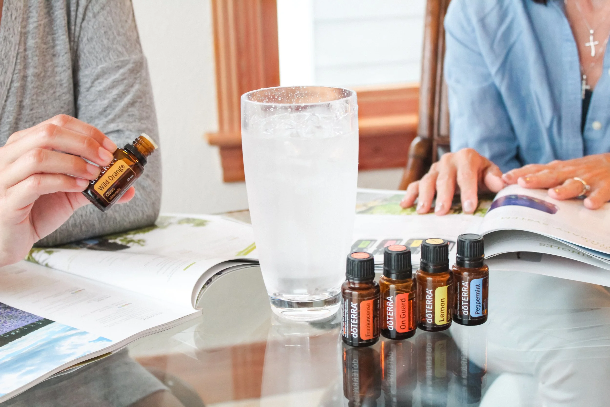 Mani di donne con brochure e boccette di oli essenziali e un grande bicchiere d'acqua ghiacciata consulente del benessere doterra