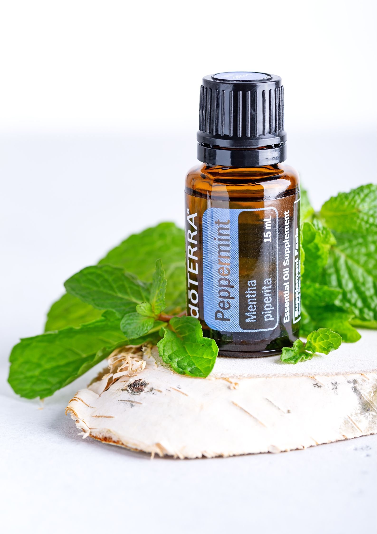 Boccetta di olio essenziale di menta piperita Peppermint doTERRA su base di legno con foglie di menta intorno - Silvia Pagliarini