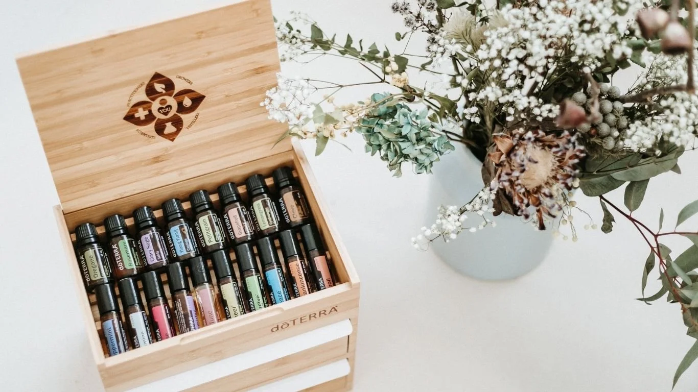 Scatola in legno con boccette di oli essenziali e fiori secchi su un tavolo bianco