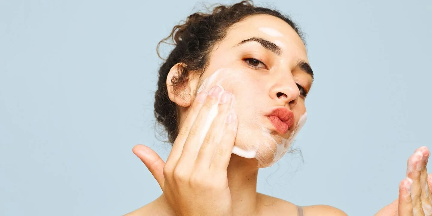 Woman washing her face with soap against a light blue background.