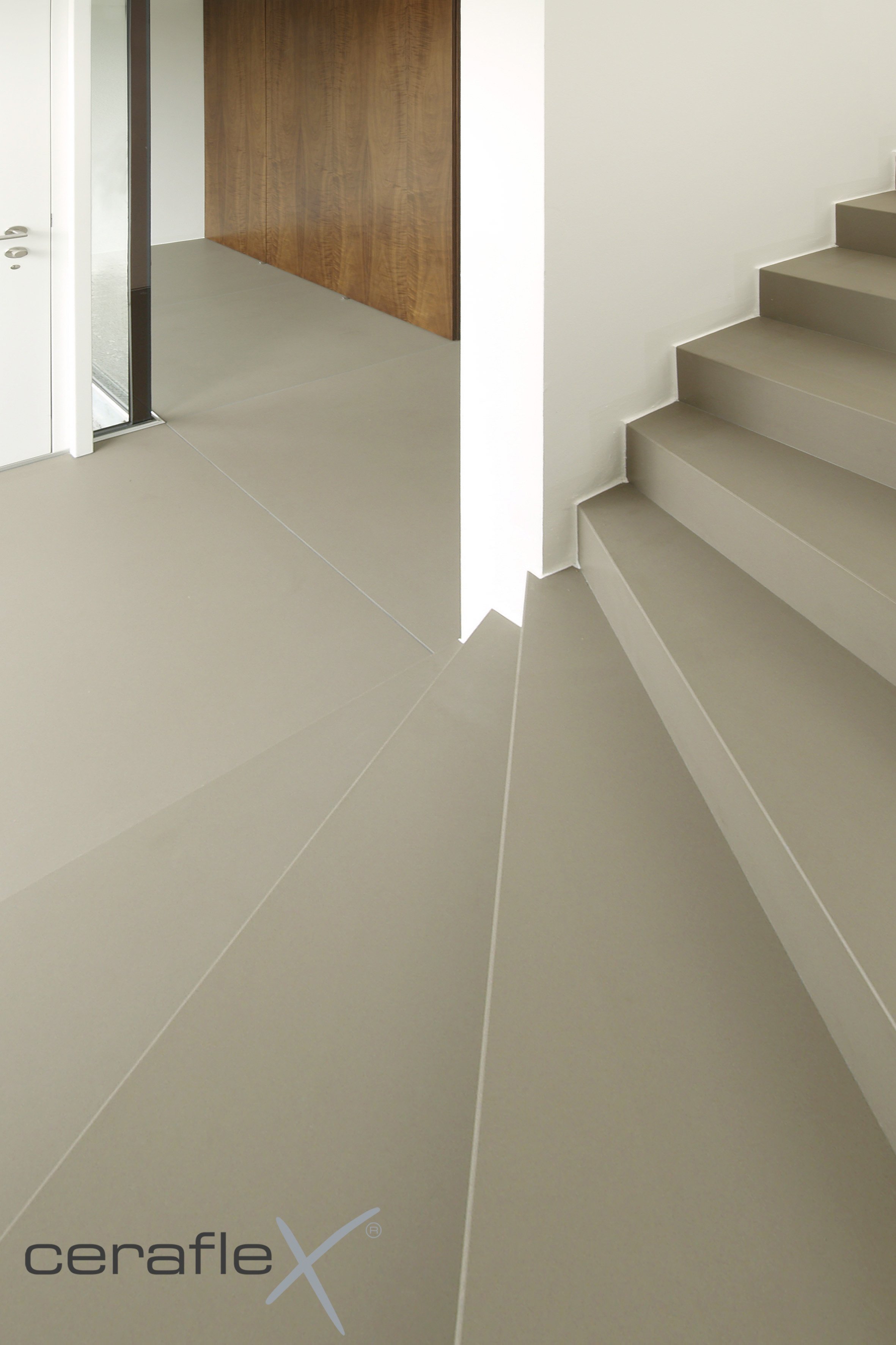 Innenaufnahme eines modernen Hauses mit beige-braunem keramischem Bodenbelag, Treppenstufen und weißer Wand, ein Holzpaneel im Hintergrund.
