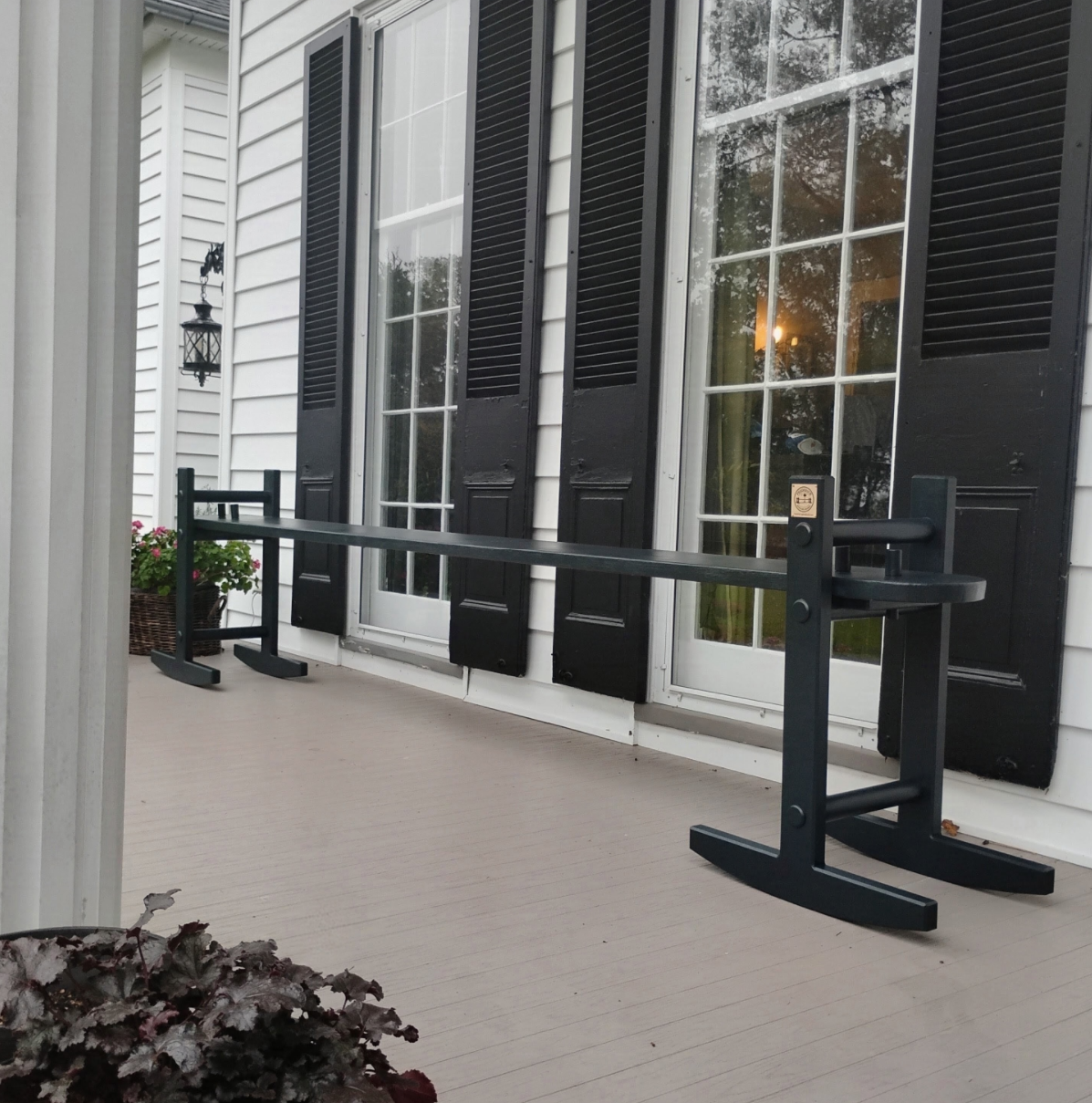 Front porch with white siding, black window shutters, glass door, potted flowers, and an empty Charleston Green bench.