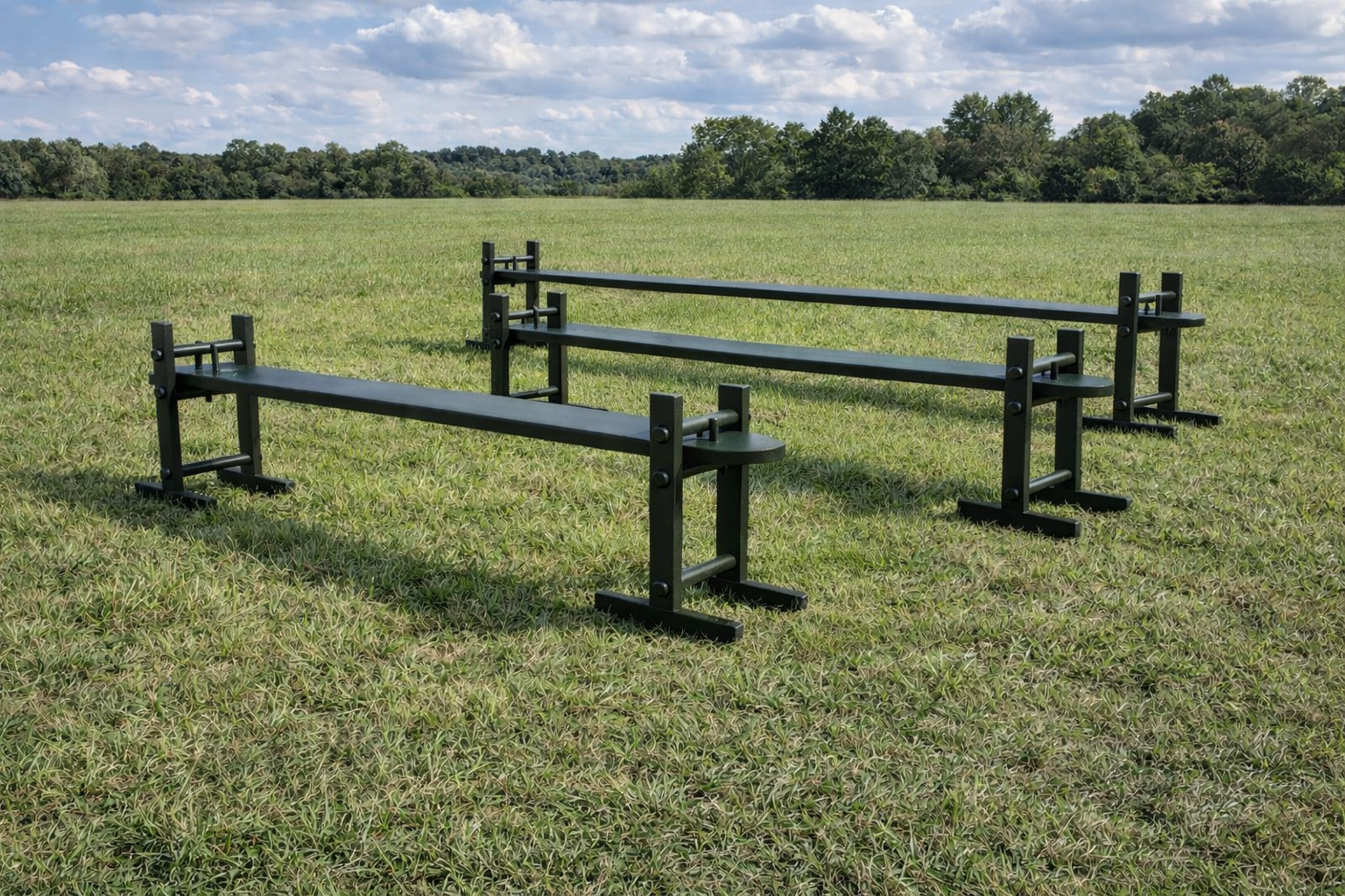 Three black metal sawhorses on a grassy field with trees and a blue sky in the background.
