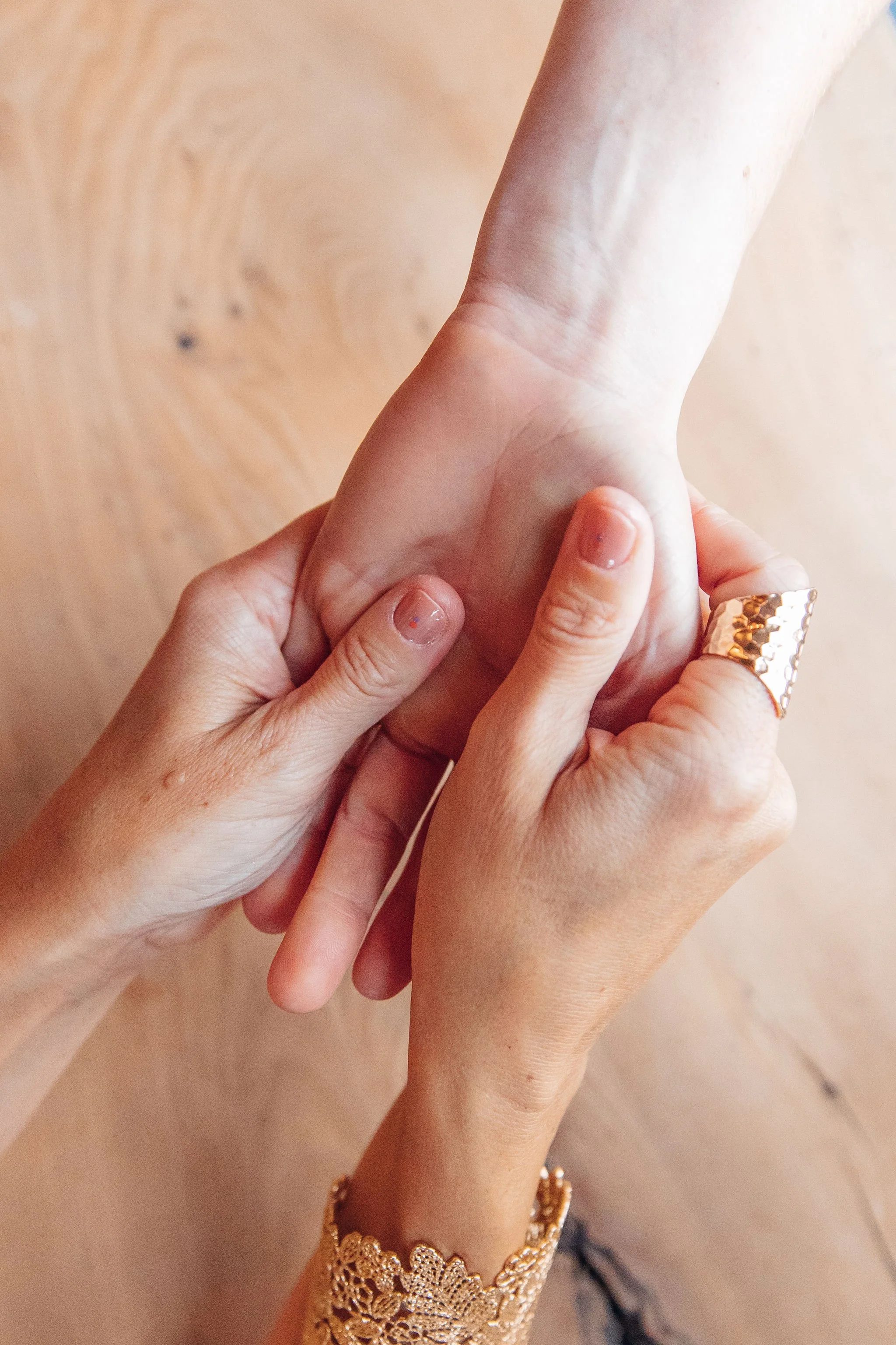 Close-up of two hands holding each other, one hand with a gold ring and a lace sleeve, the other hand's fingernails are painted with chipped nail polish.