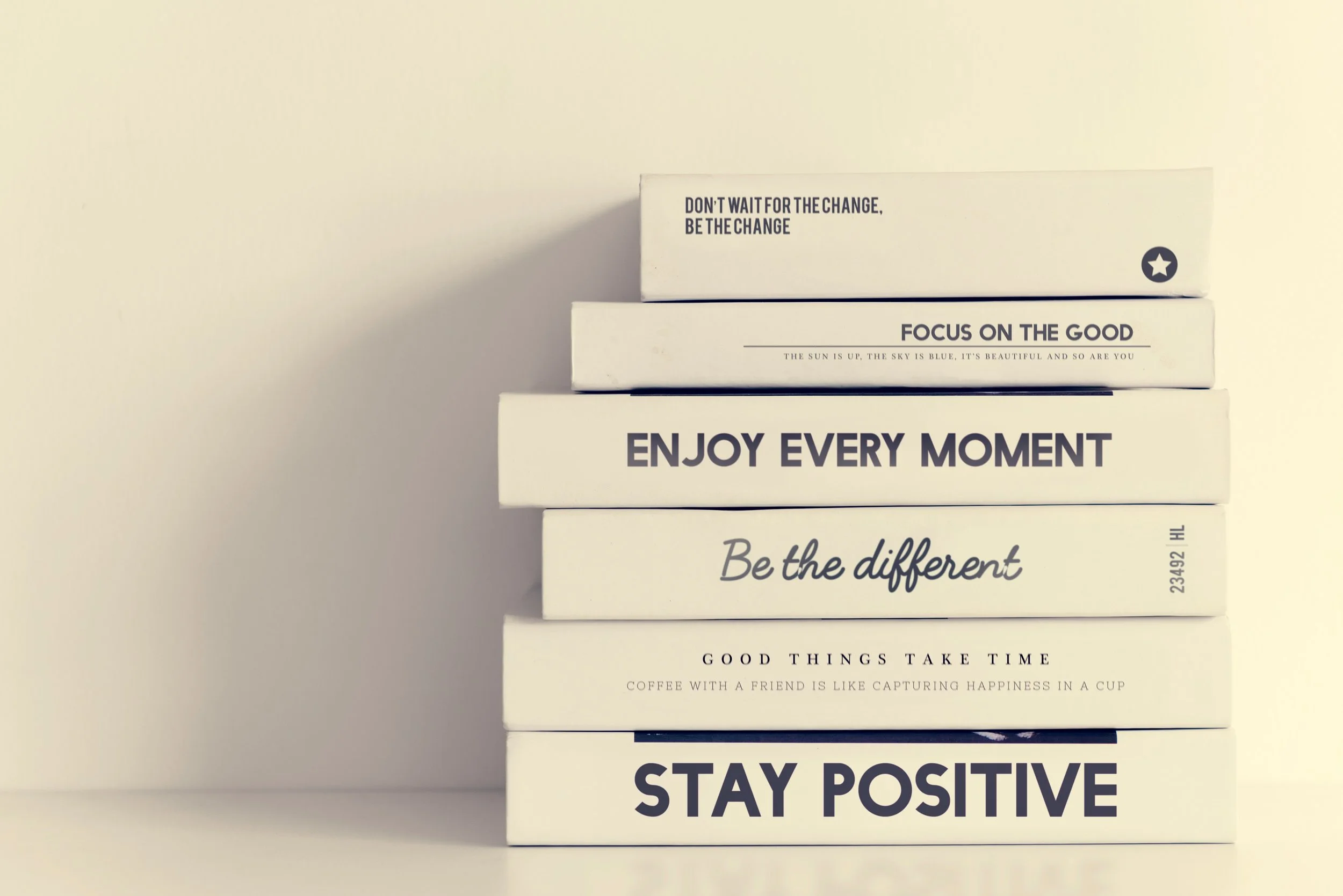 Stack of white books with motivational quotes on a beige wall.