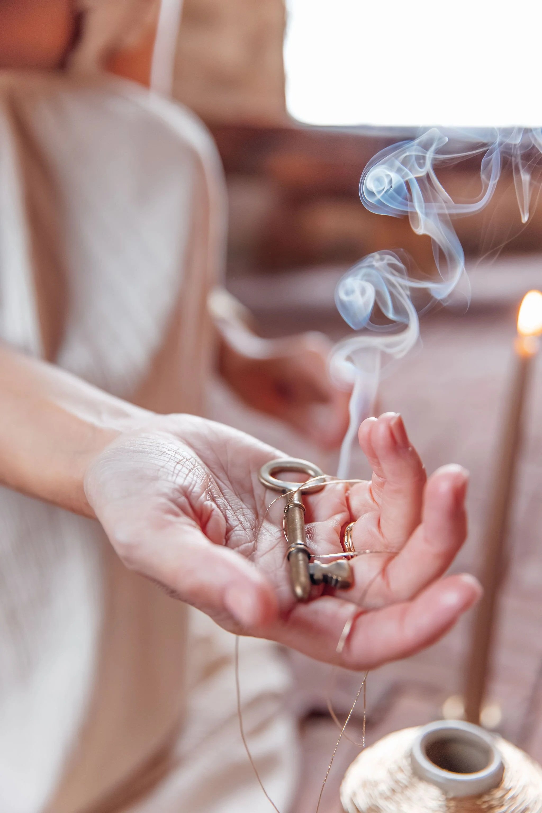 Close-up of a person's hand holding vintage keys, with smoke rising from an incense or candle in the background.