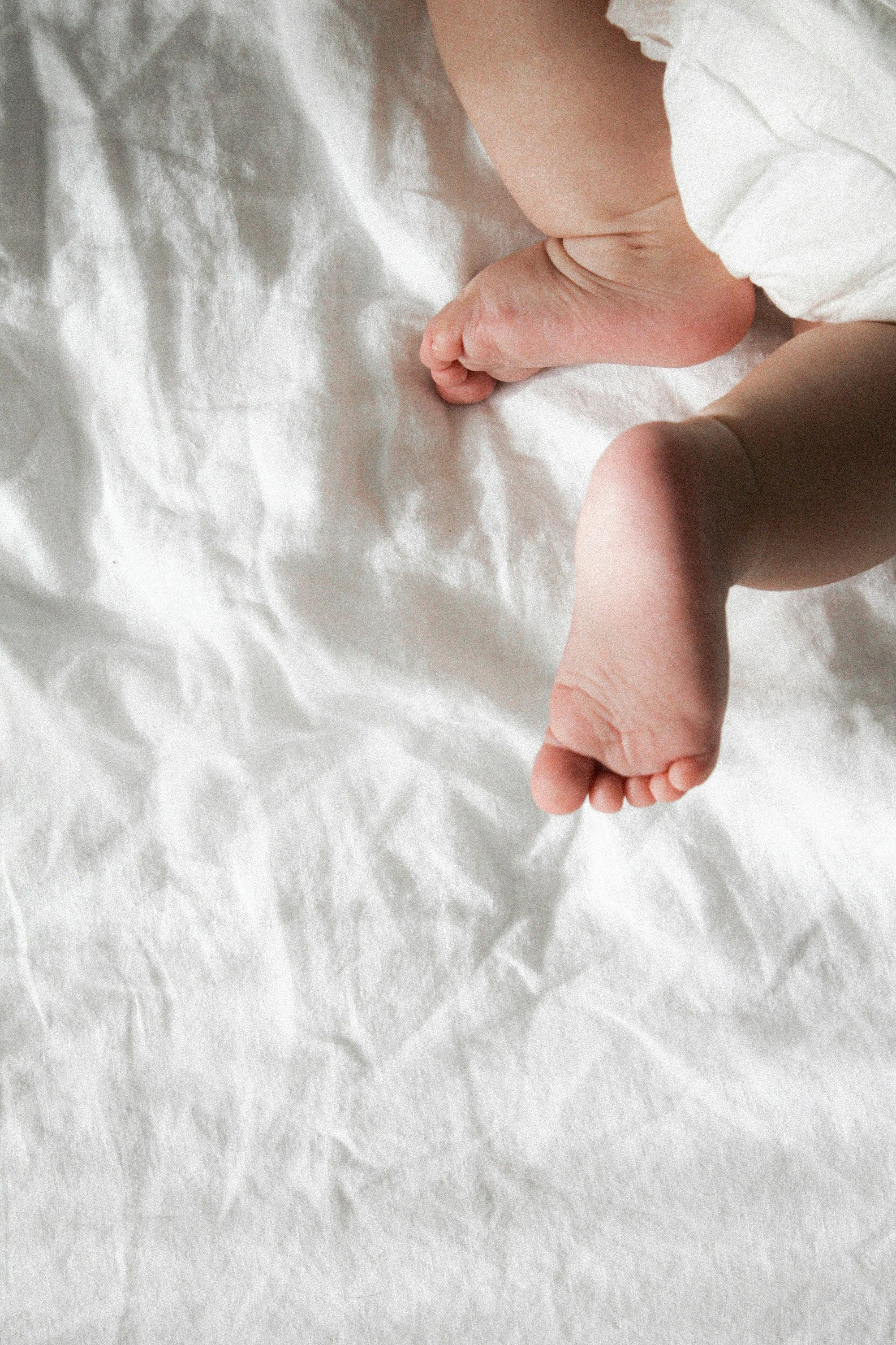 Close-up of a baby's feet on a white crinkled sheet, showing tiny toes and soft skin.