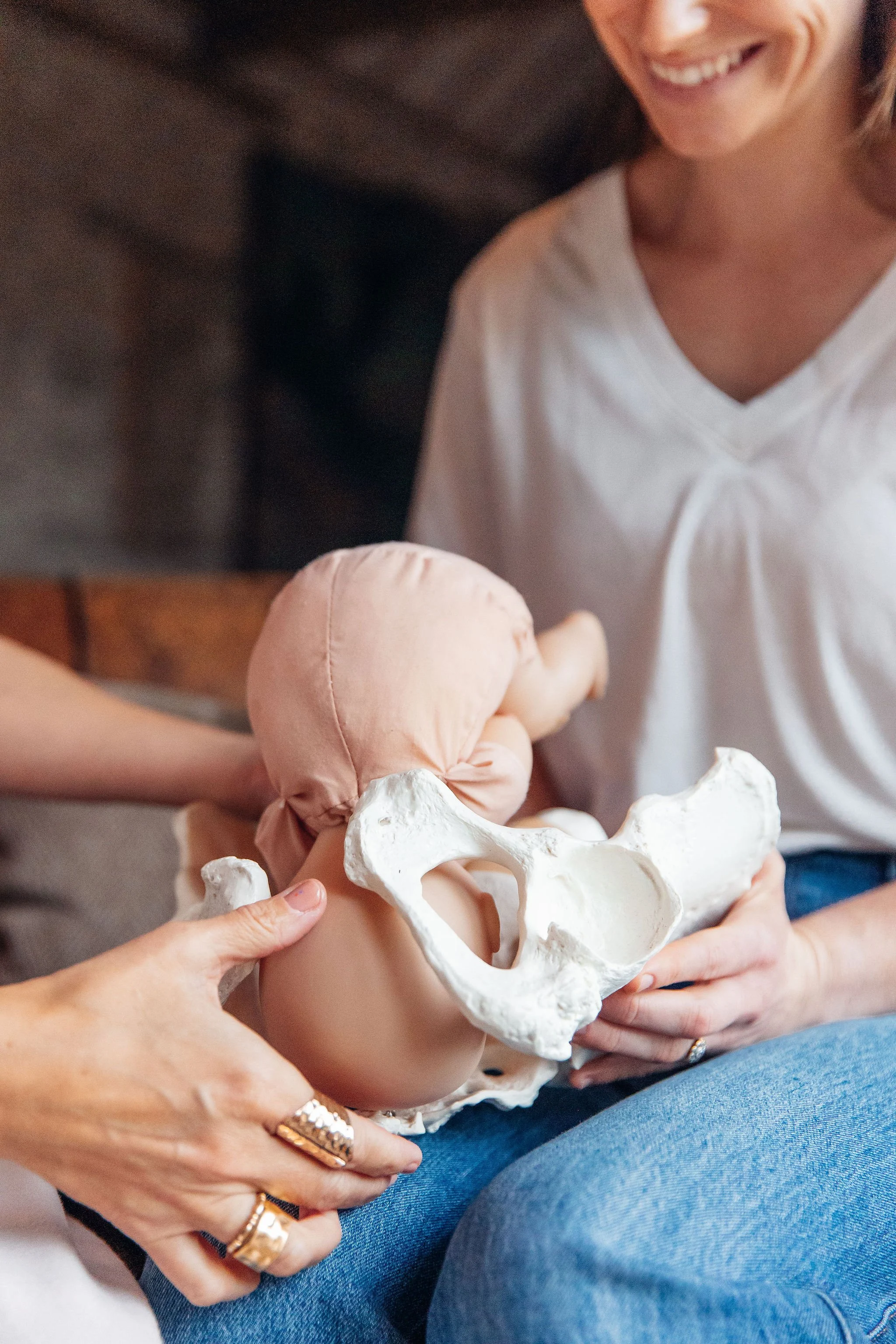 Woman holding a pelvis model with a baby in cloth wrap, sitting on her lap.