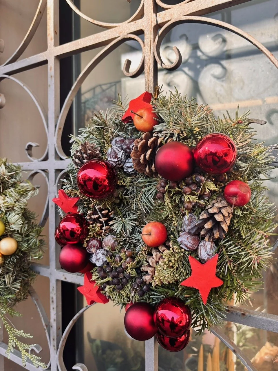 Corona dell'Avvento decorata con rami di pino, pigne, bacche rosse e sfere rosse lucide.