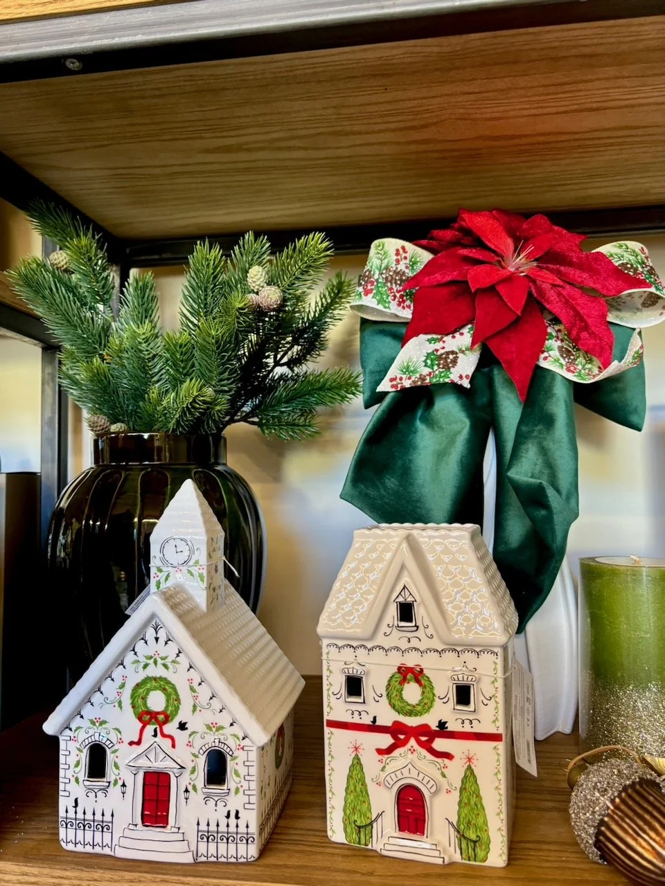 Decorazioni natalizie con casette di ceramica, un vaso con rami di abete decorati per il Natale, e un grande fiocco rosso con dettagli natalizi