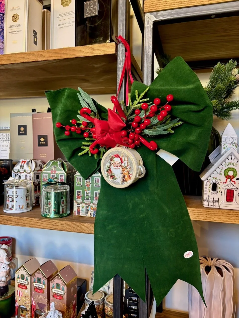 Ghirlanda natalizia con grandi foglie di pino, bacche rosse, fiocco rosso e un ornamento con Babbo Natale e una renna, appesa a una scaffalatura in un negozio