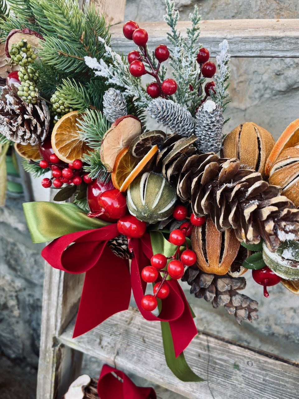 Corona natalizia decorata con rami di pino, bacche rosse, agrumi secchi, pigne, ed altre decorazioni verdi e rosse.