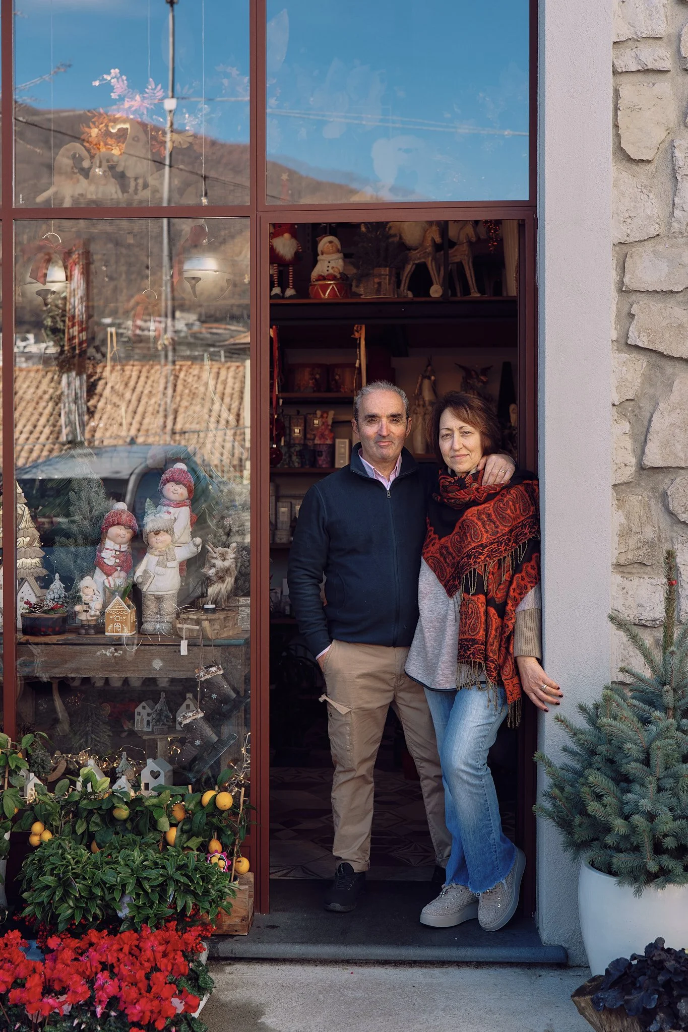 Una coppia di persone si trova all'ingresso di un negozio decorato per il Natale, con ornamenti e luci festose.