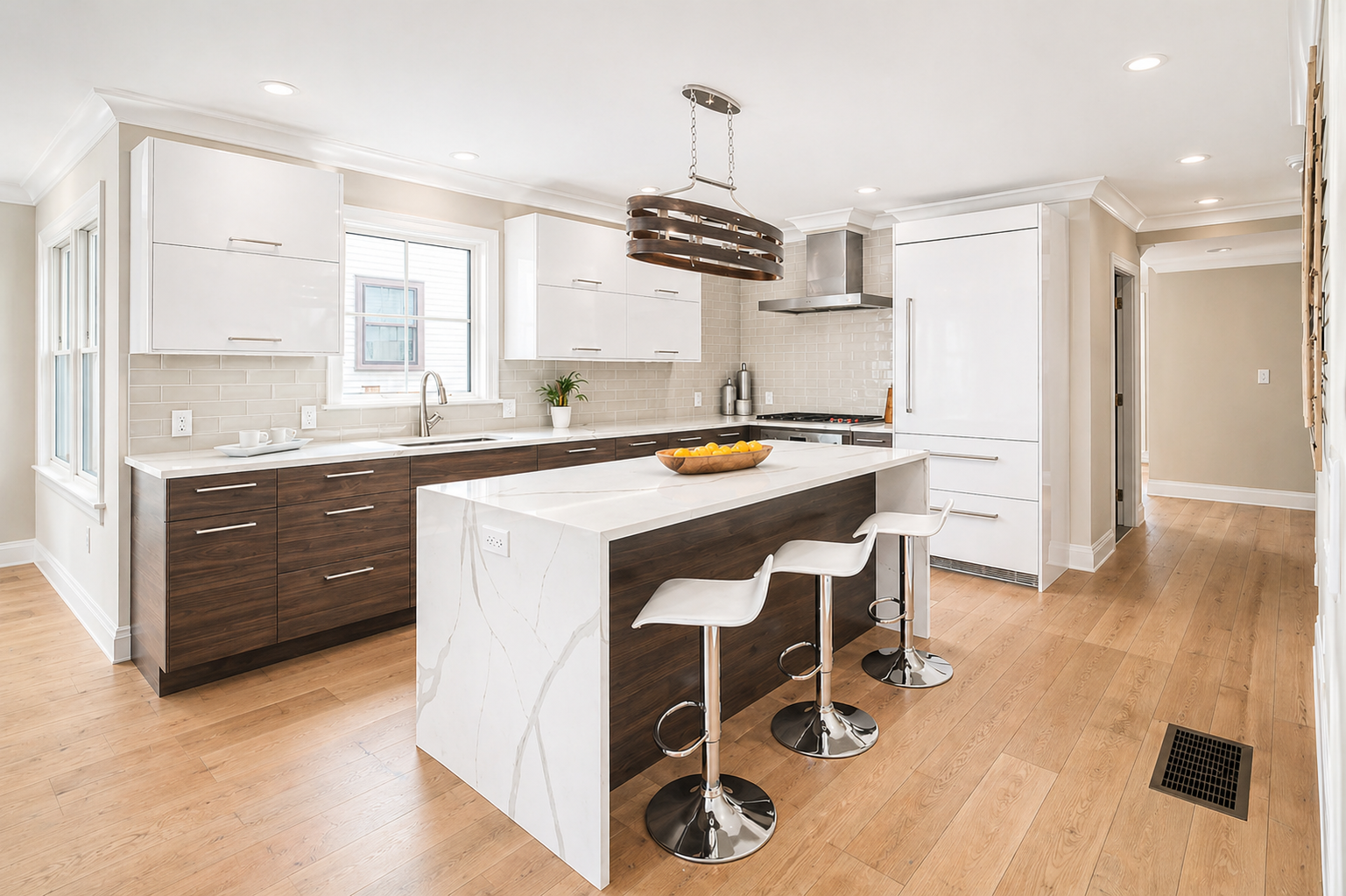 Modern kitchen with white upper cabinets, dark lower cabinets, a white marble island with a dark wood panel, and light wood flooring. Features include a window above the sink, a hanging light fixture, and barstools at the island.