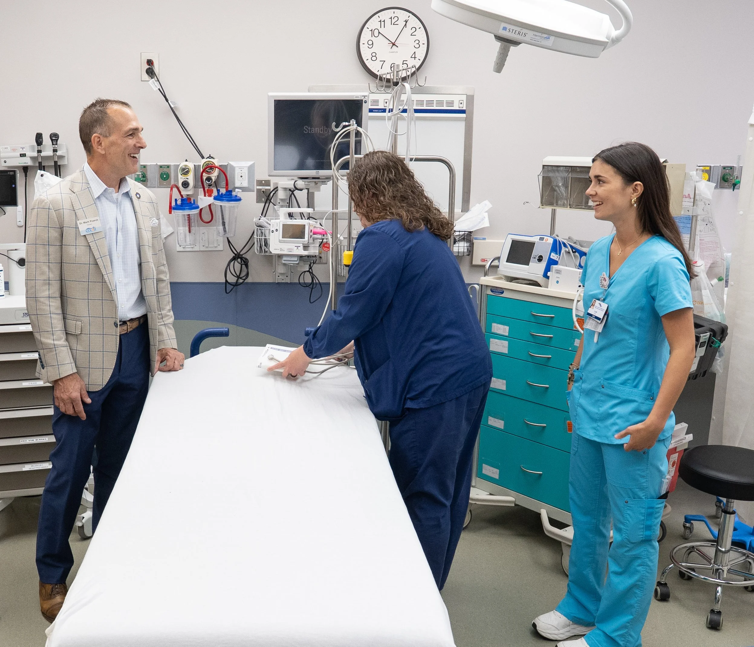 Three people standing in an ER room around and empty bed. Two of them are looking at each other smiling.