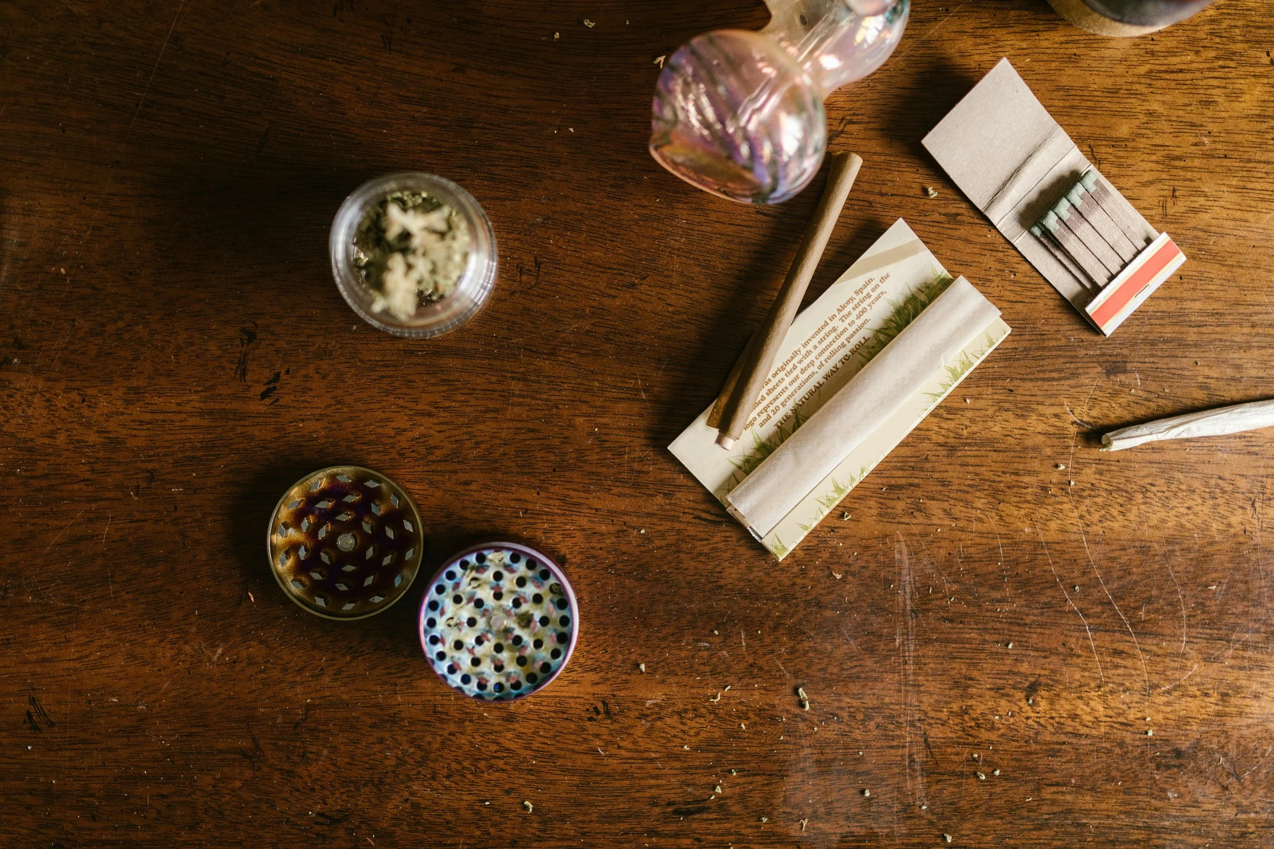 flat lay image showing wood table, cannabis accessories, papers, matches and cannabis