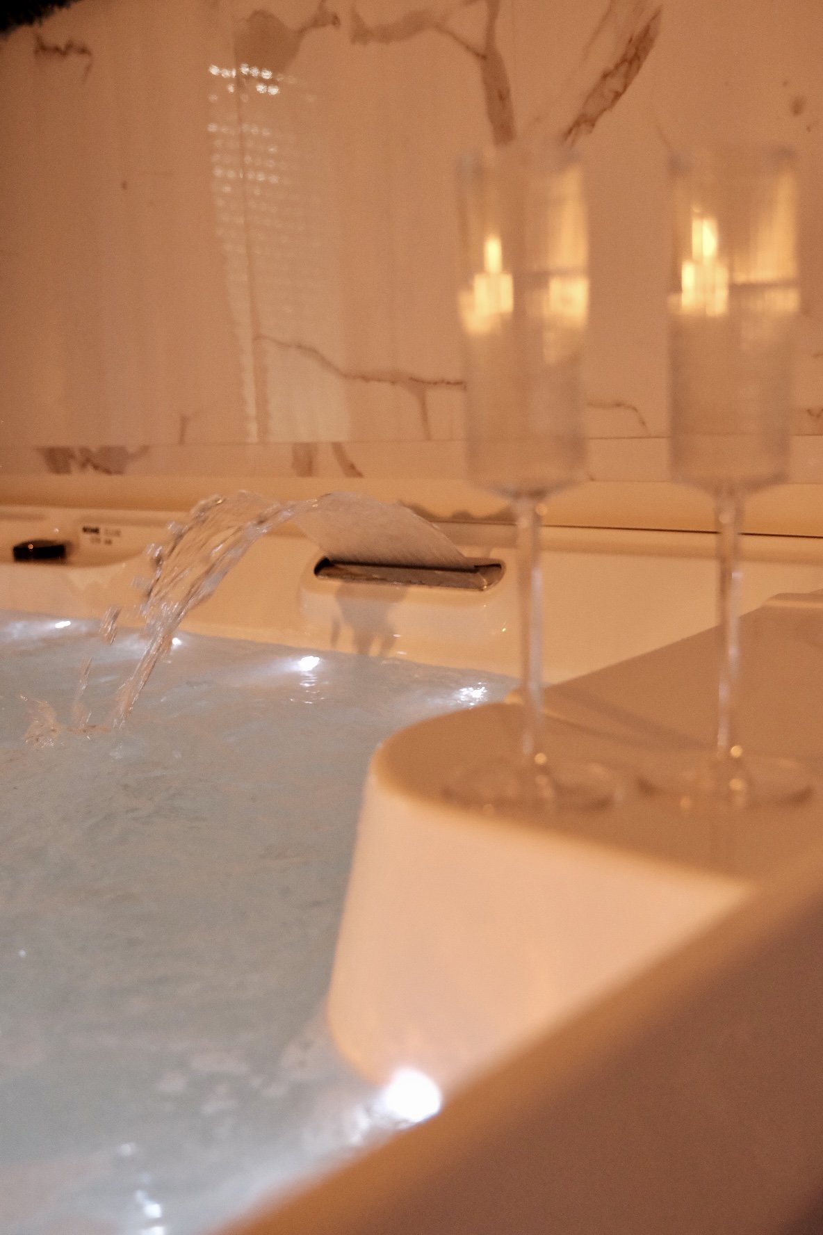 Détail d'une baignoire avec de l'eau qui coule et un porte-candles avec trois bougies allumées.