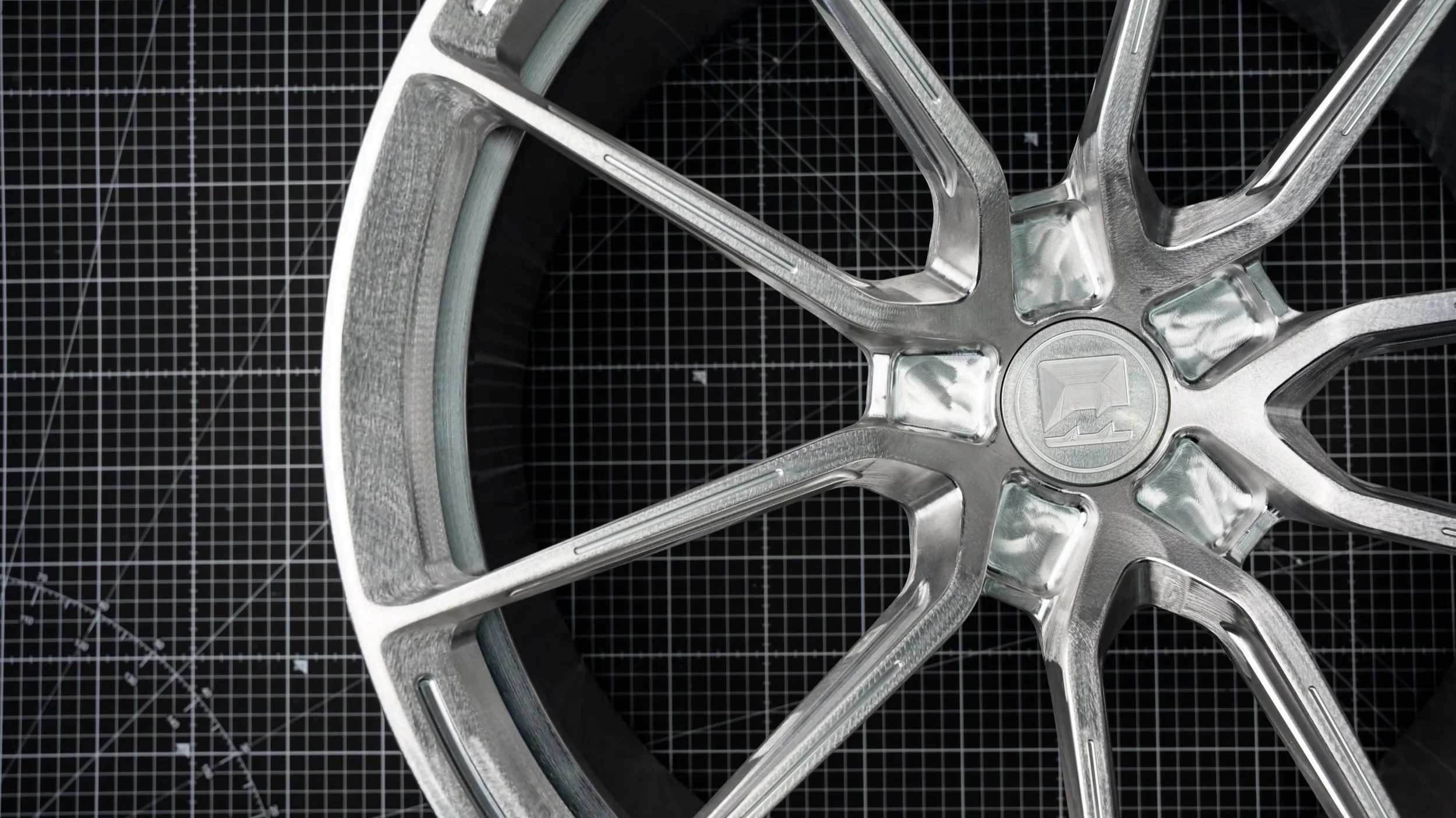 Close-up of a metallic car wheel rim on a black grid cutting mat.