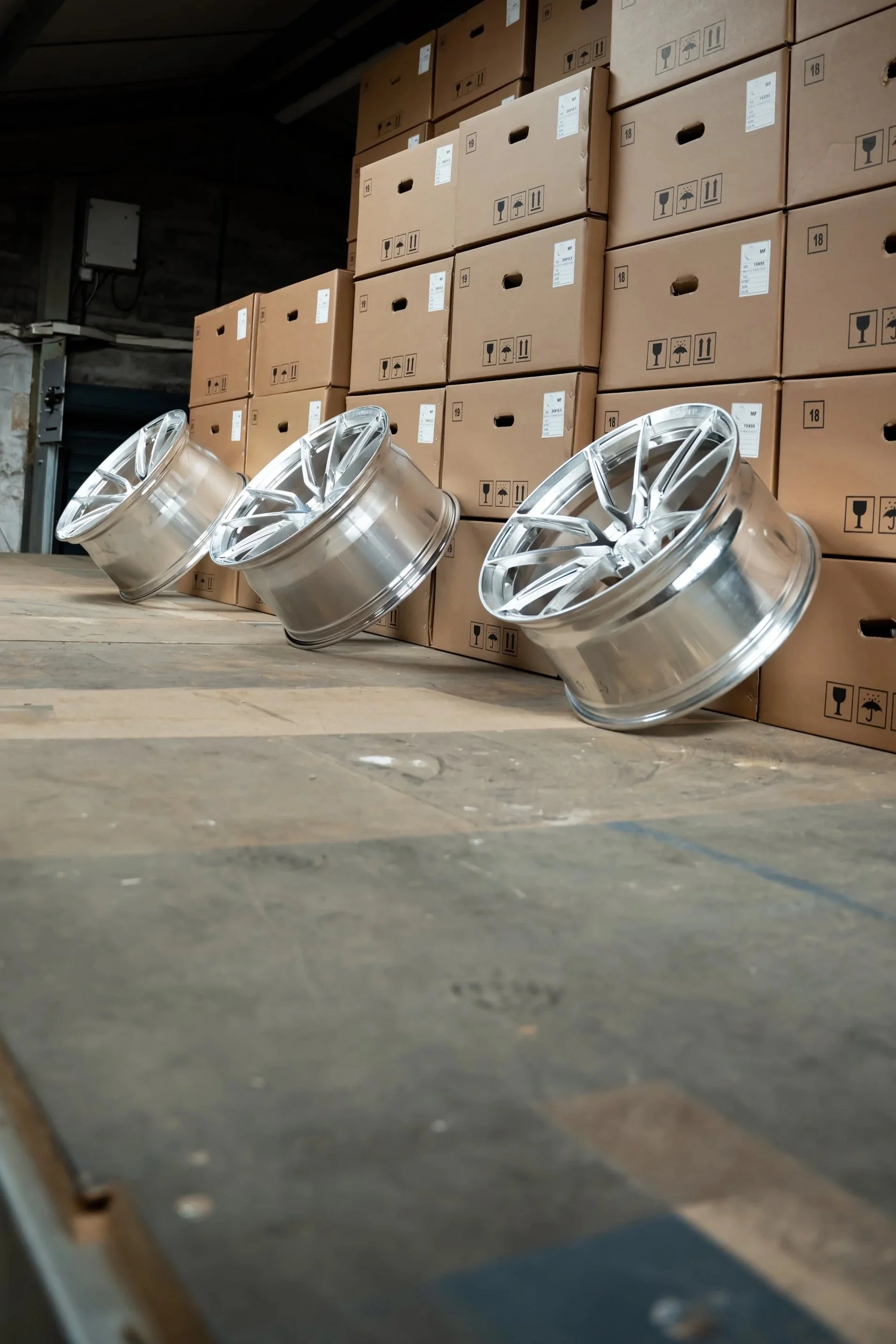 Three car rims on a wooden table with cardboard boxes stacked in the background.