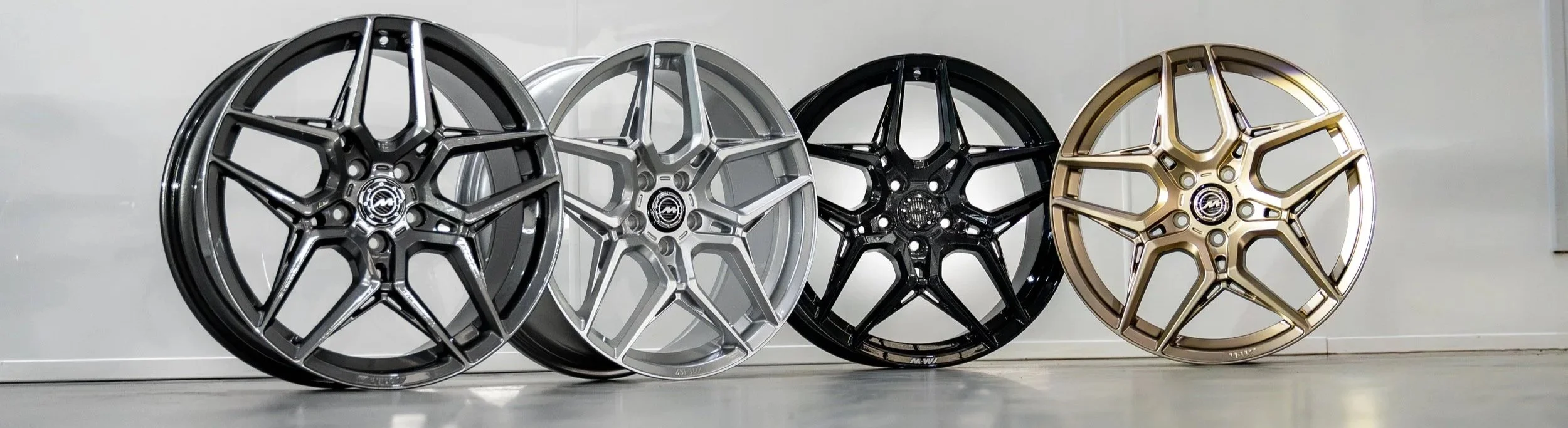 Four luxury car wheels in black, silver, gray, and gold finishes are displayed against a plain white background.