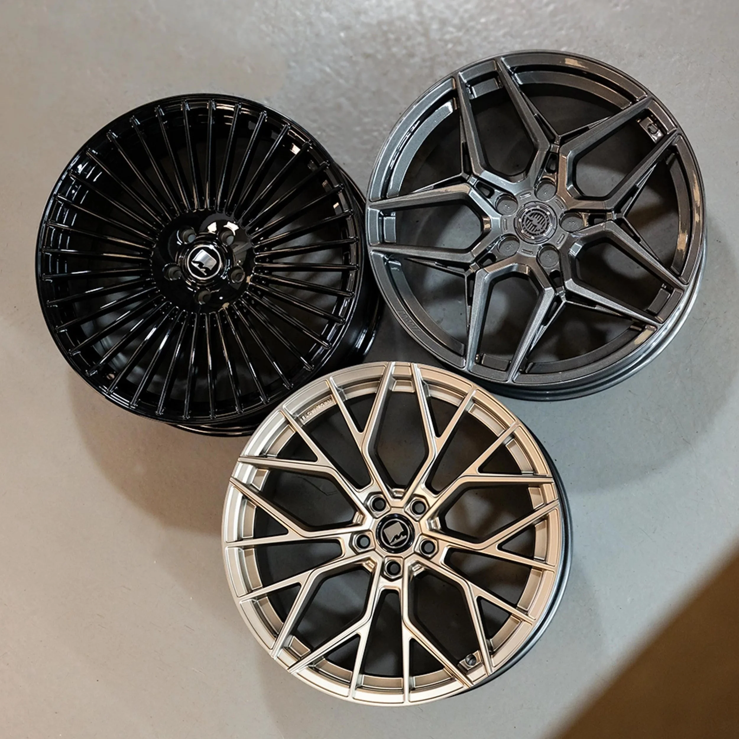 Three car wheels with intricate spoke designs. One is black, one is silver, and one is dark gray.