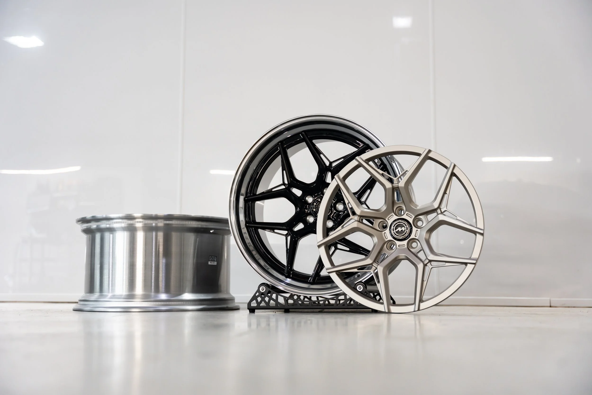 Two car wheels, one black and one silver, standing vertically, with a silver rim on the left side, placed on a flat white surface against a white wall.