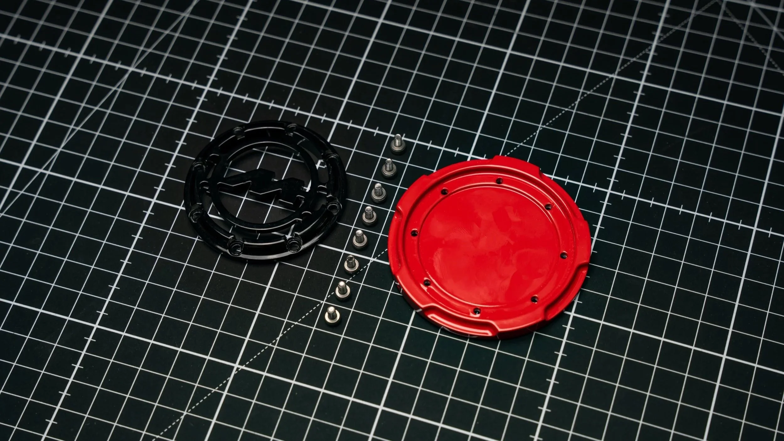 Disassembled red and black fuel cap with screws on a cutting mat.