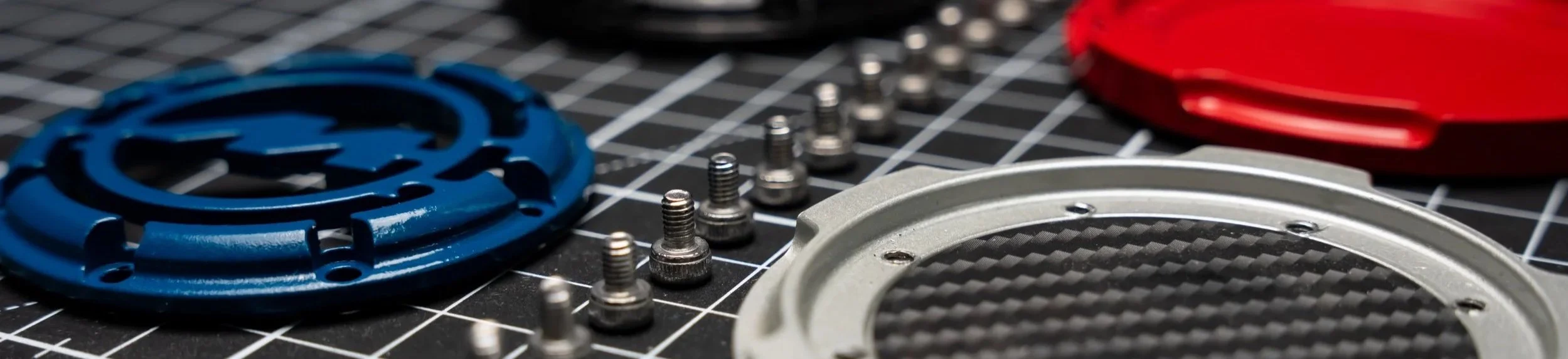 Close-up of colorful mechanical parts, screws, and metal components on a black grid work surface.
