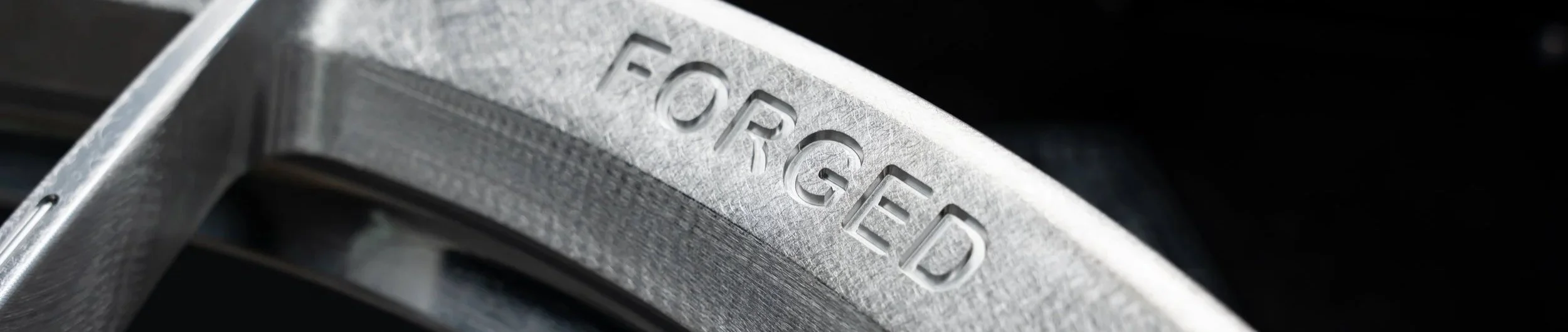 Close-up of a metallic wheel rim with the brand name "FORGED" engraved on it.