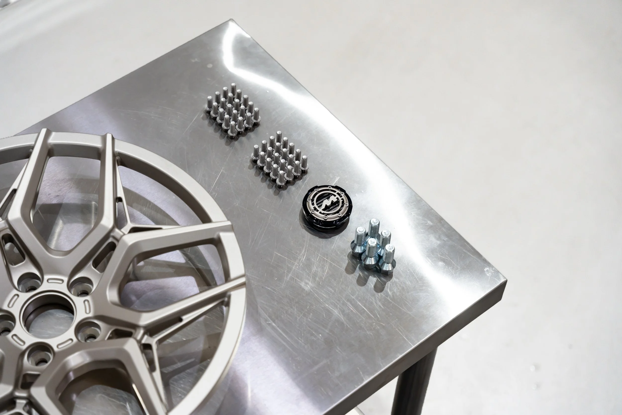 A metallic table with a bicycle disc brake rotor, two sets of silver screws, a small black circular object, and a silver component on a metal table.