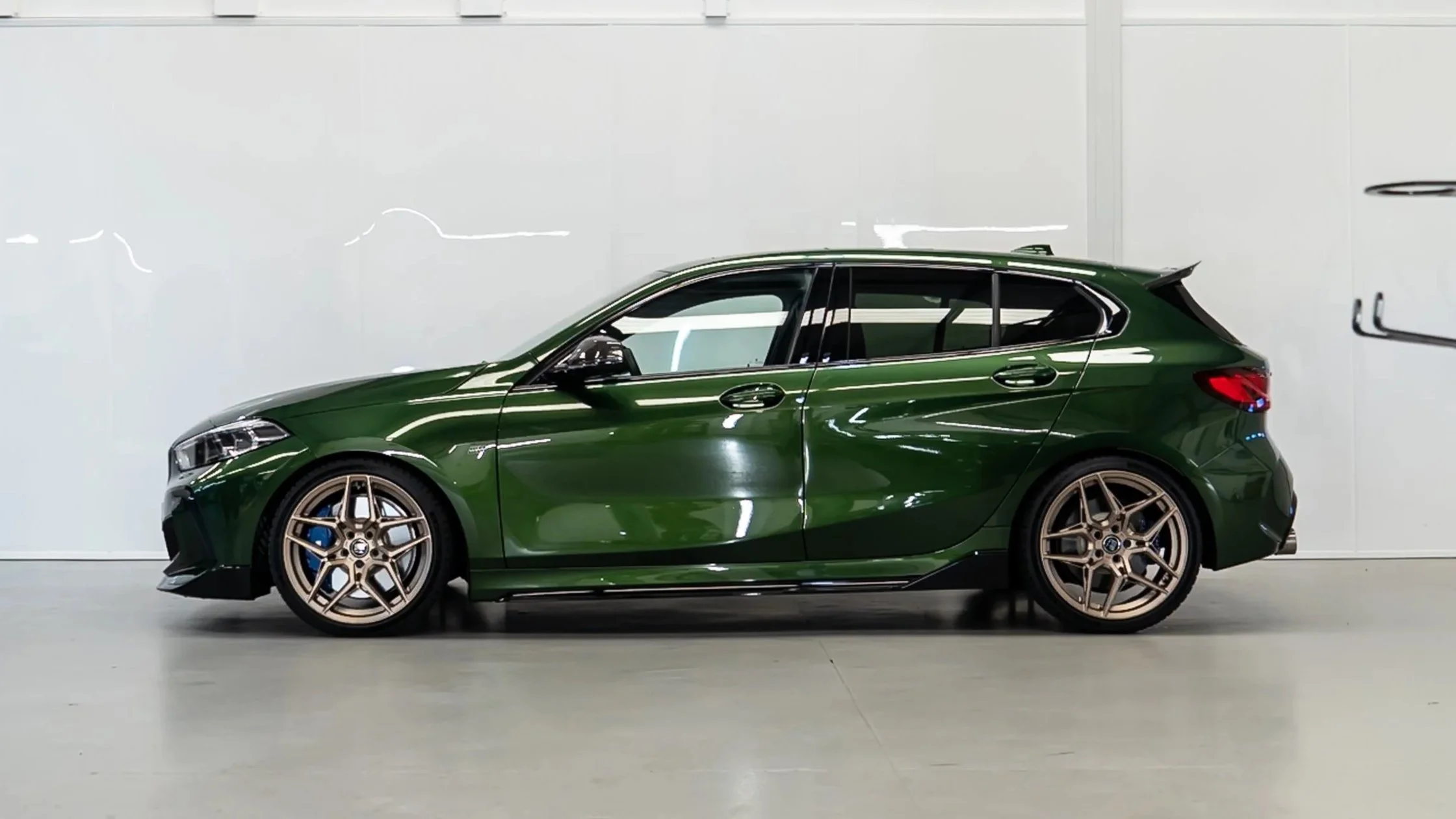 Green hatchback car parked indoors with white walls and smooth floor.