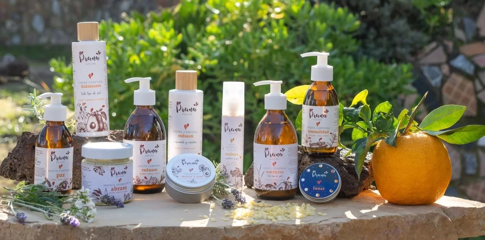 Variedad de productos de cuidado personal con ingredientes naturales, incluyendo aceites, cremas y un frasco con una naranja y hojas verdes, en un entorno al aire libre.