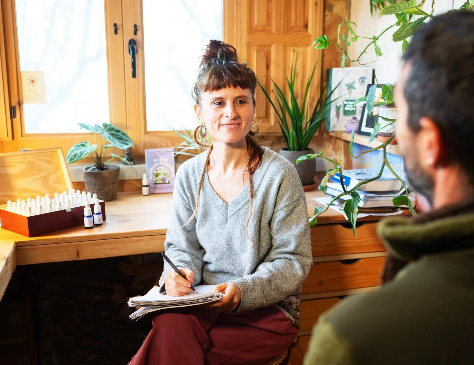 Mujer realizando una consulta con un terapeuta en una oficina de estilo rústico con plantas y libros en el fondo.