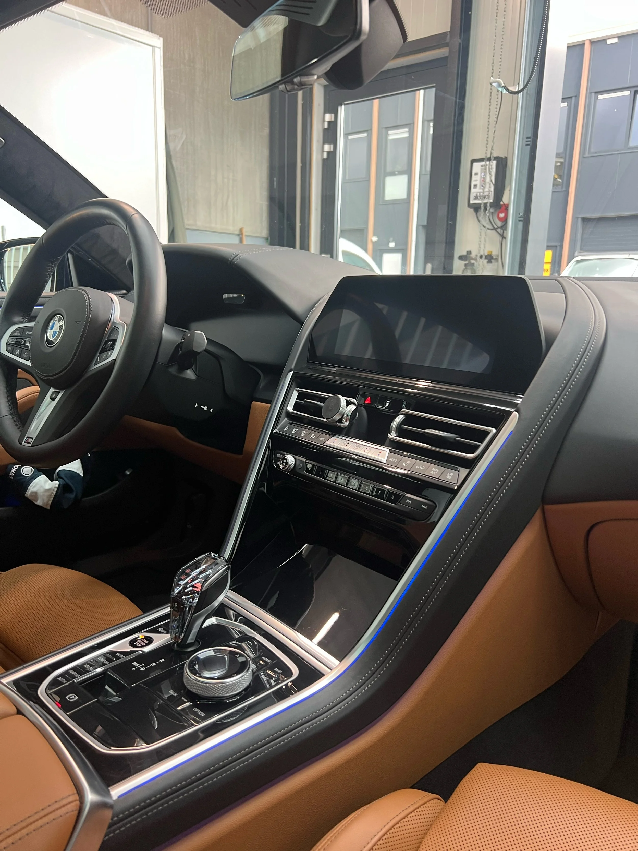 The interior of a modern BMW vehicle showing the dashboard, steering wheel, center console with gear shifter, and an infotainment screen.