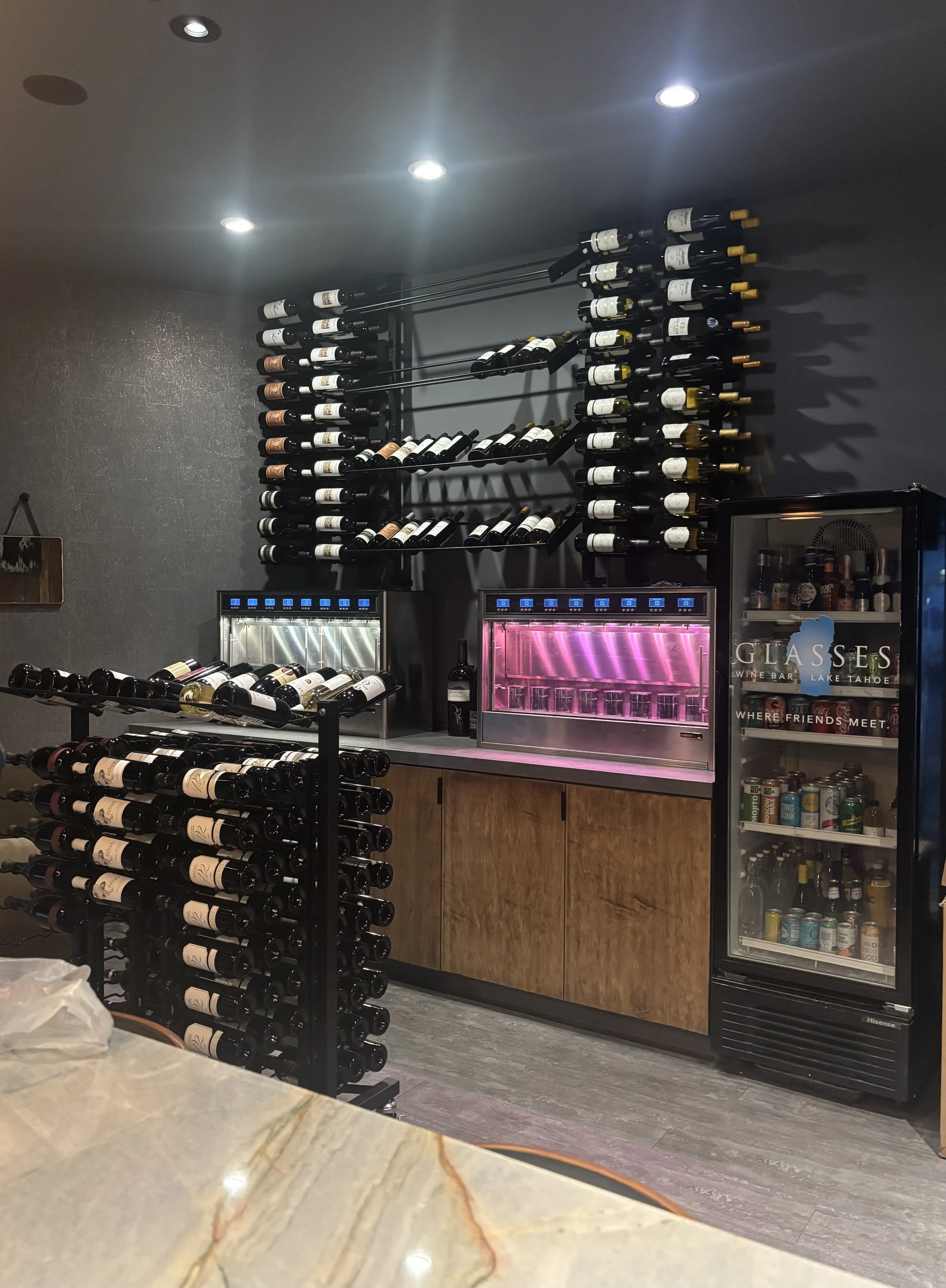 Wine bottles on racks and a refrigerator with drinks in a bar setting.