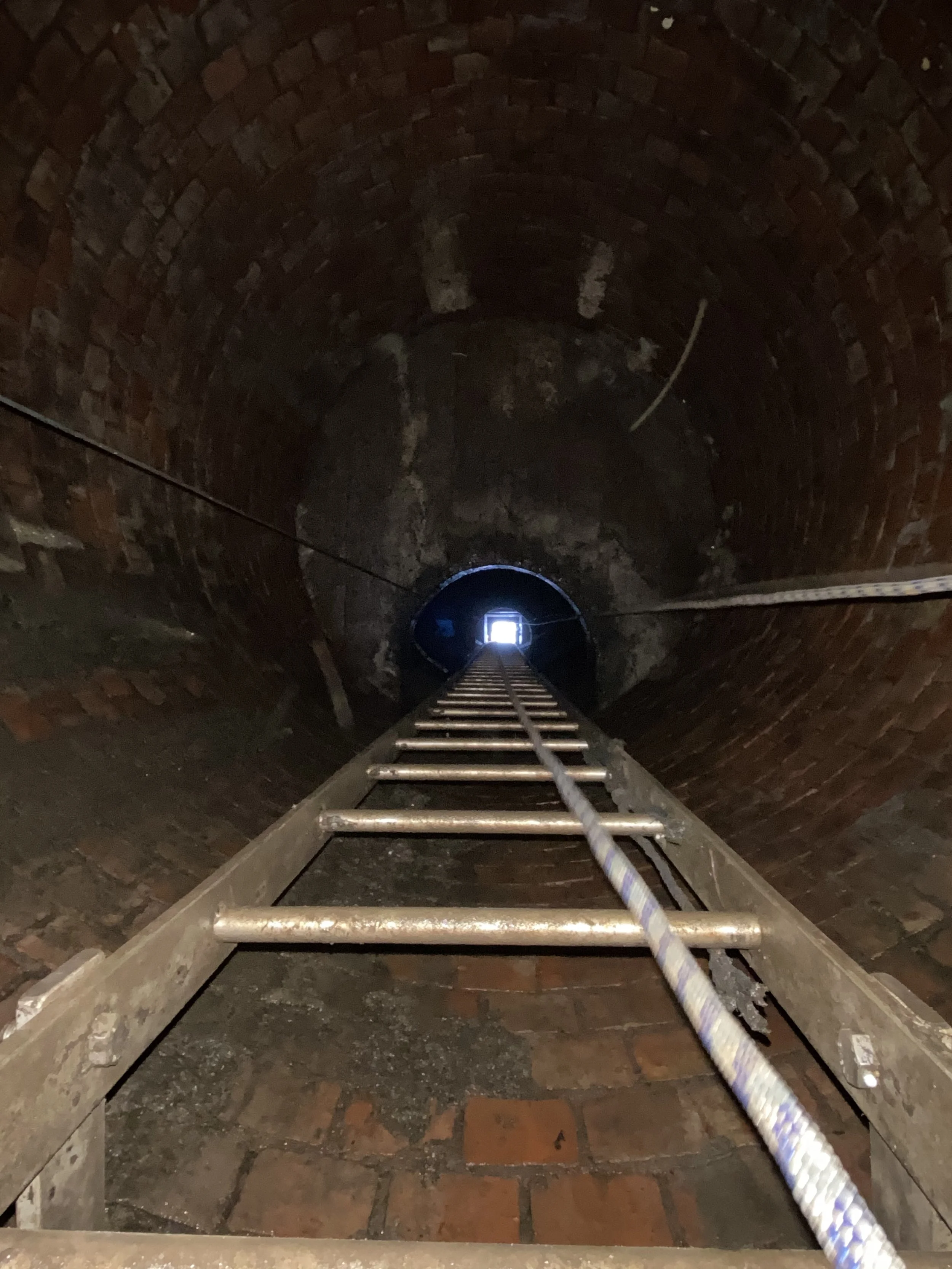 Inside a brick chimney with a ladder and rope leading up to a small square opening at the top.