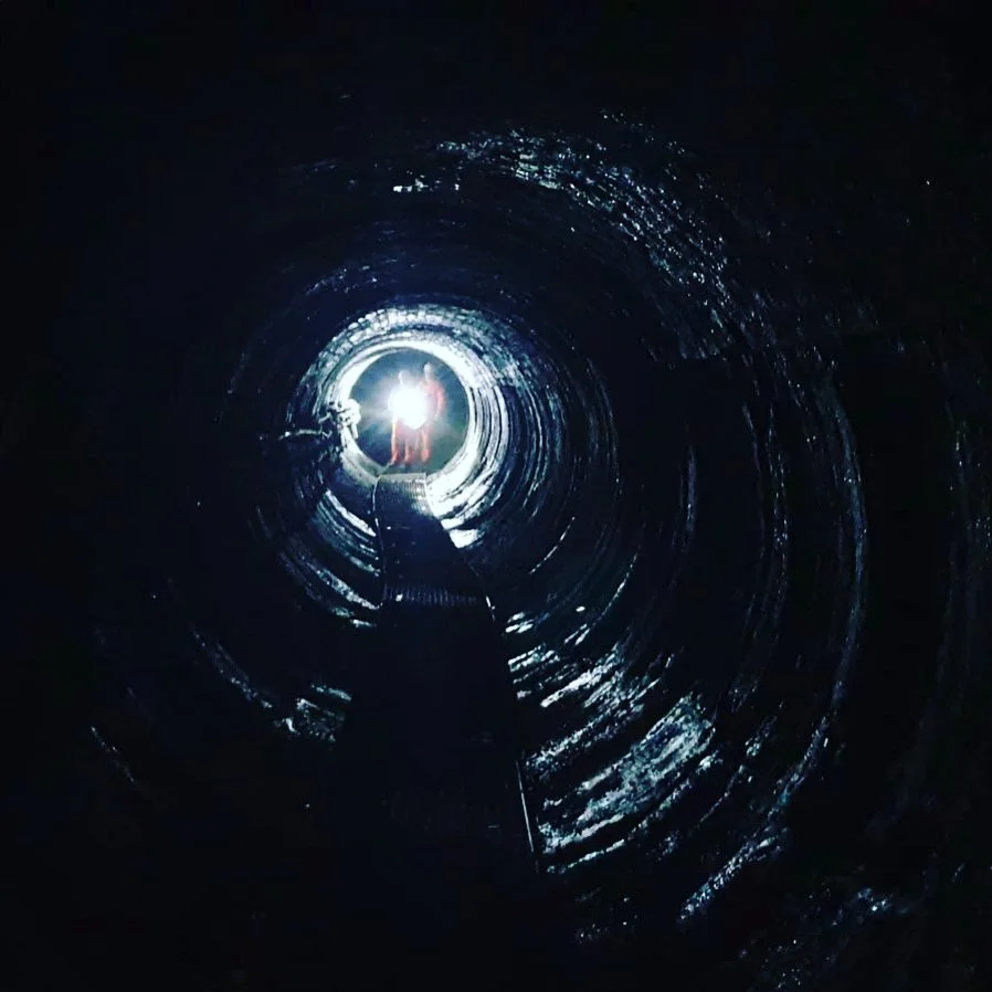 A person climbing inside a dark, cylindrical tunnel with a light at the end.