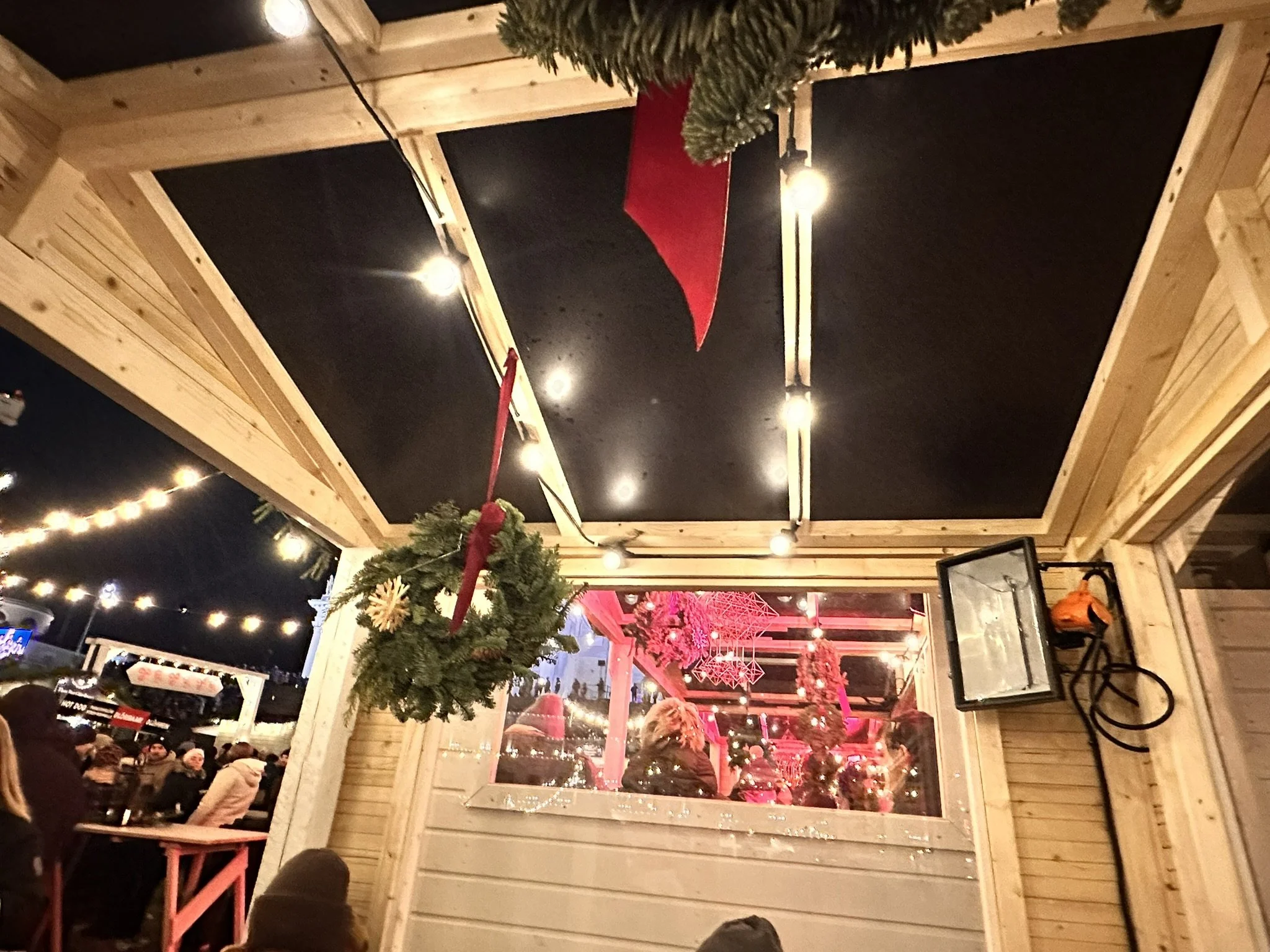 Wooden market stall with electric heater, Christmas greenery, and festive lights at Tuomaan Markkinat Christmas market in Helsinki Senate Square